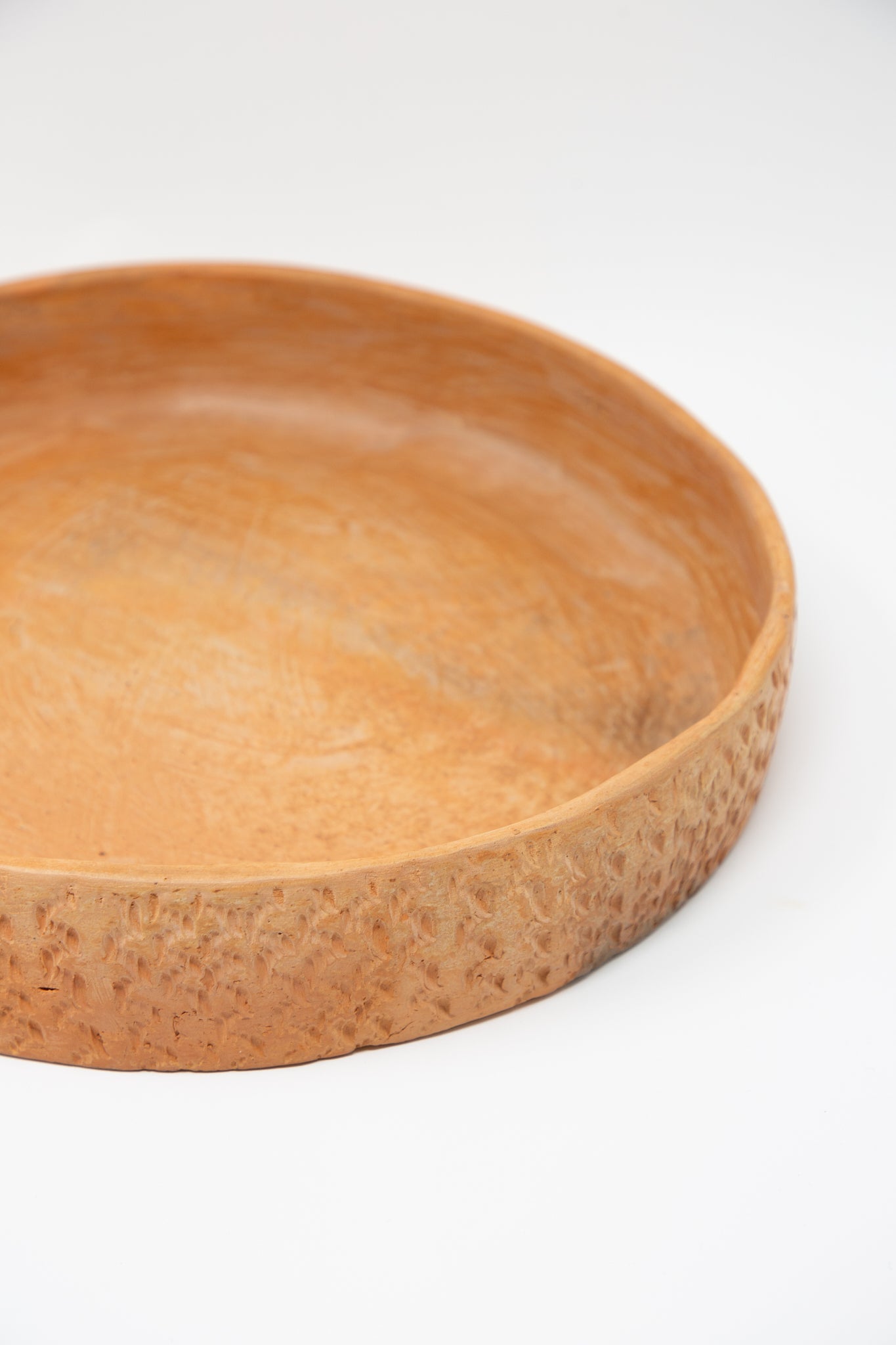 A Julia Frutero Platter in Red Clay from Plaza Bolivar, a rustic bowl with a terracotta red clay finish, is placed on a white surface.
