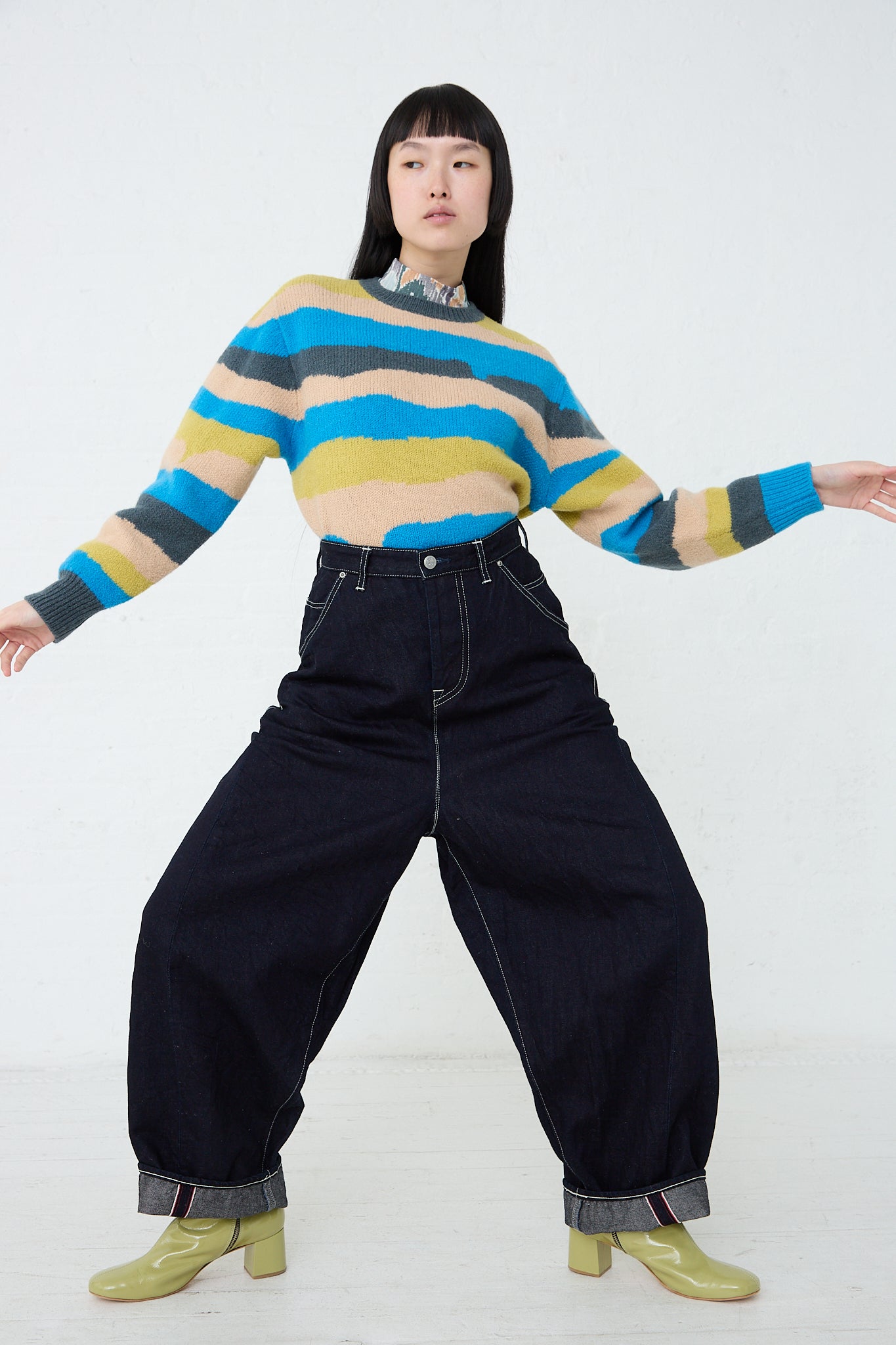 Description: A woman wearing the Mina Perhonen Always Balloon Wide Pant in Indigo and a striped sweater. Full length and front view. Model's arms are raised.