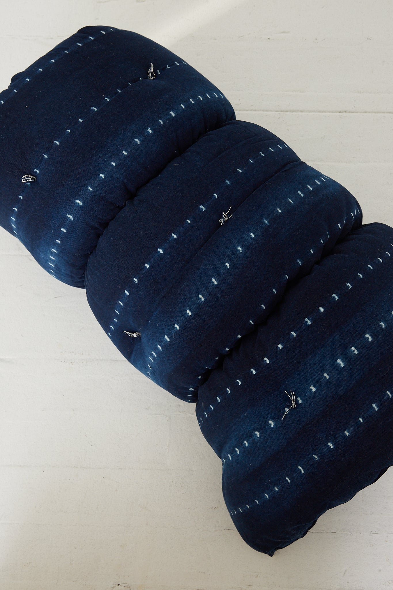 A Tensira Tufted Overlay Mattress in Dark Indigo Tie Dye pillow made of cotton, laying on a wooden floor.