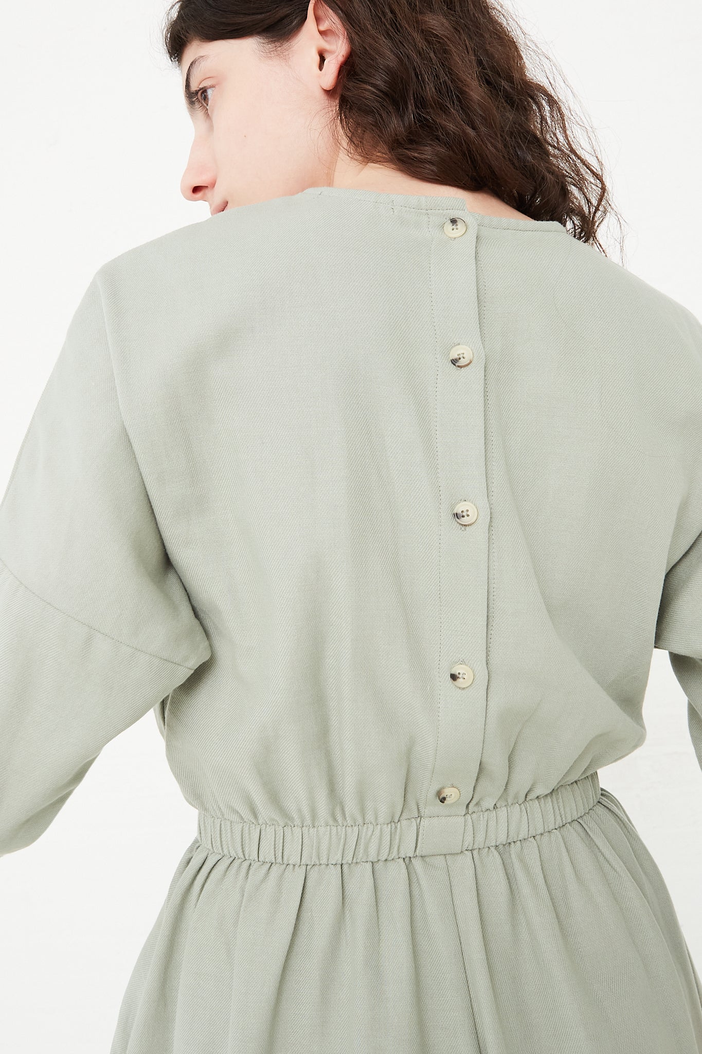 The back view of a woman wearing a Black Crane Cotton Twill Wide Culotte Jumpsuit in Agave. Up close and back view.