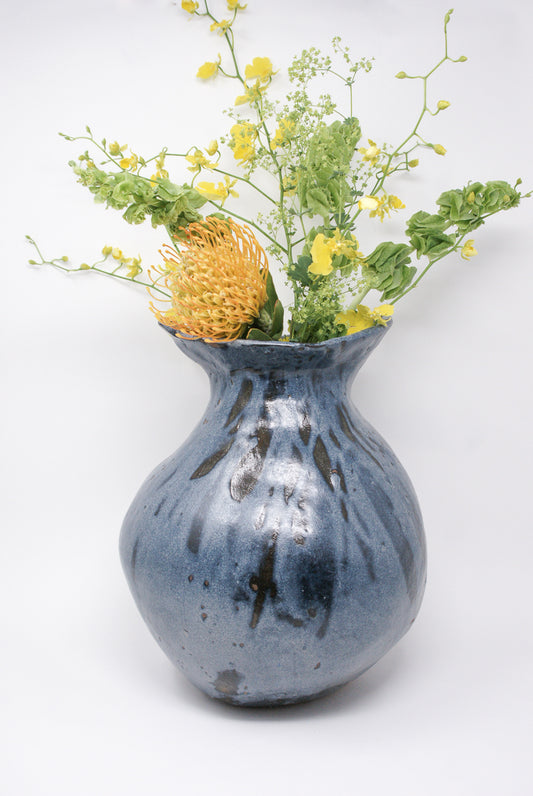 A MONDAYS Cloud-Blue Coiled Vessel in Blue Shino Glaze on Red Stoneware with yellow flowers in it.