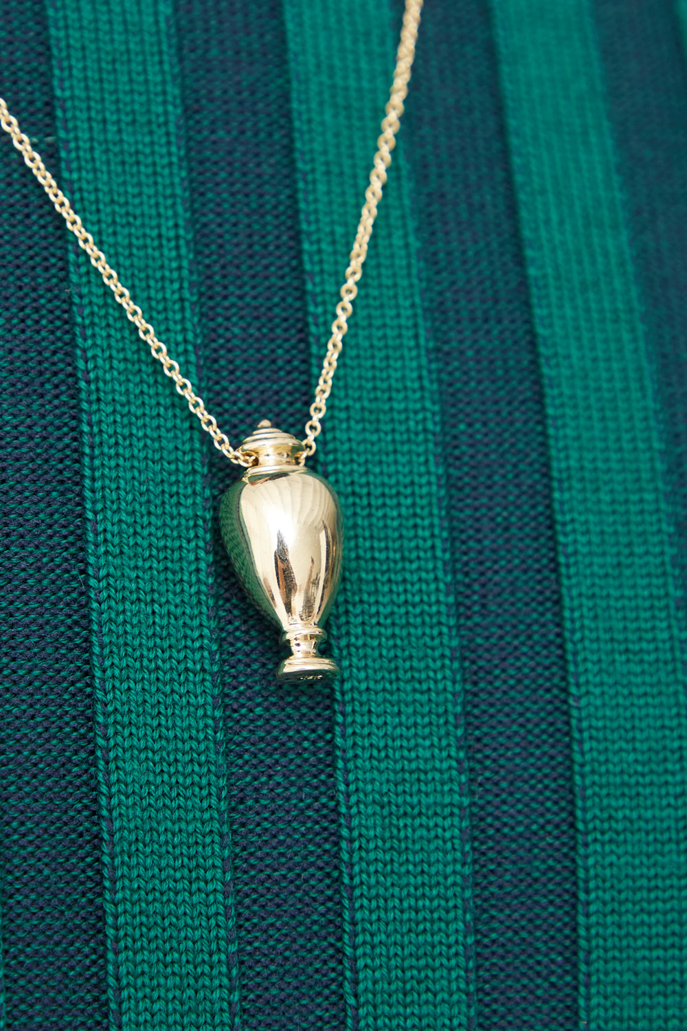 A handmade Kathryn Bentley 14K yellow gold urn pendant on a green striped sweater, crafted in Los Angeles.