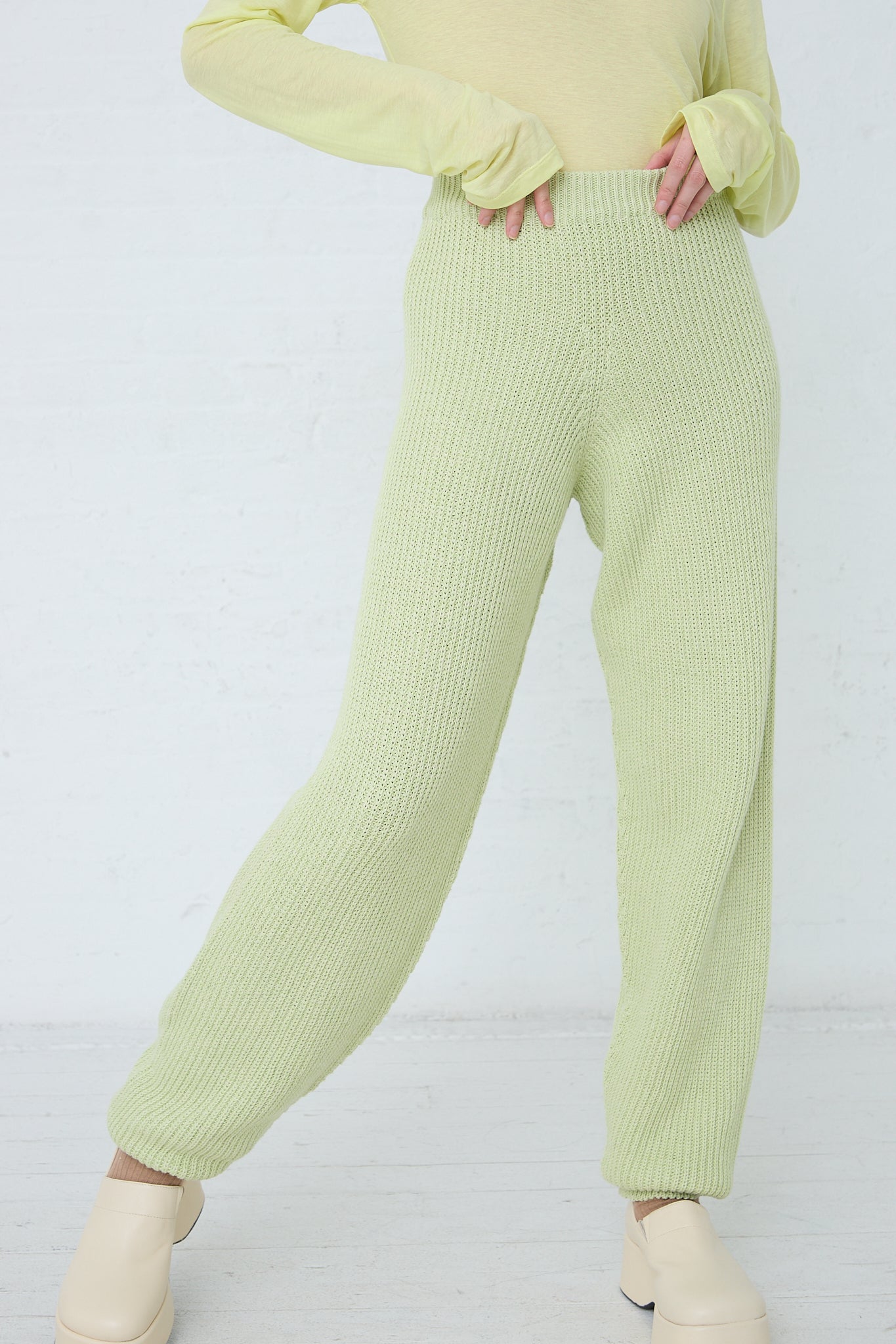 The model is wearing a sustainably produced lime sweater and green pants made from organic Cotton Dodd Pant in Mimosa by Baserange.