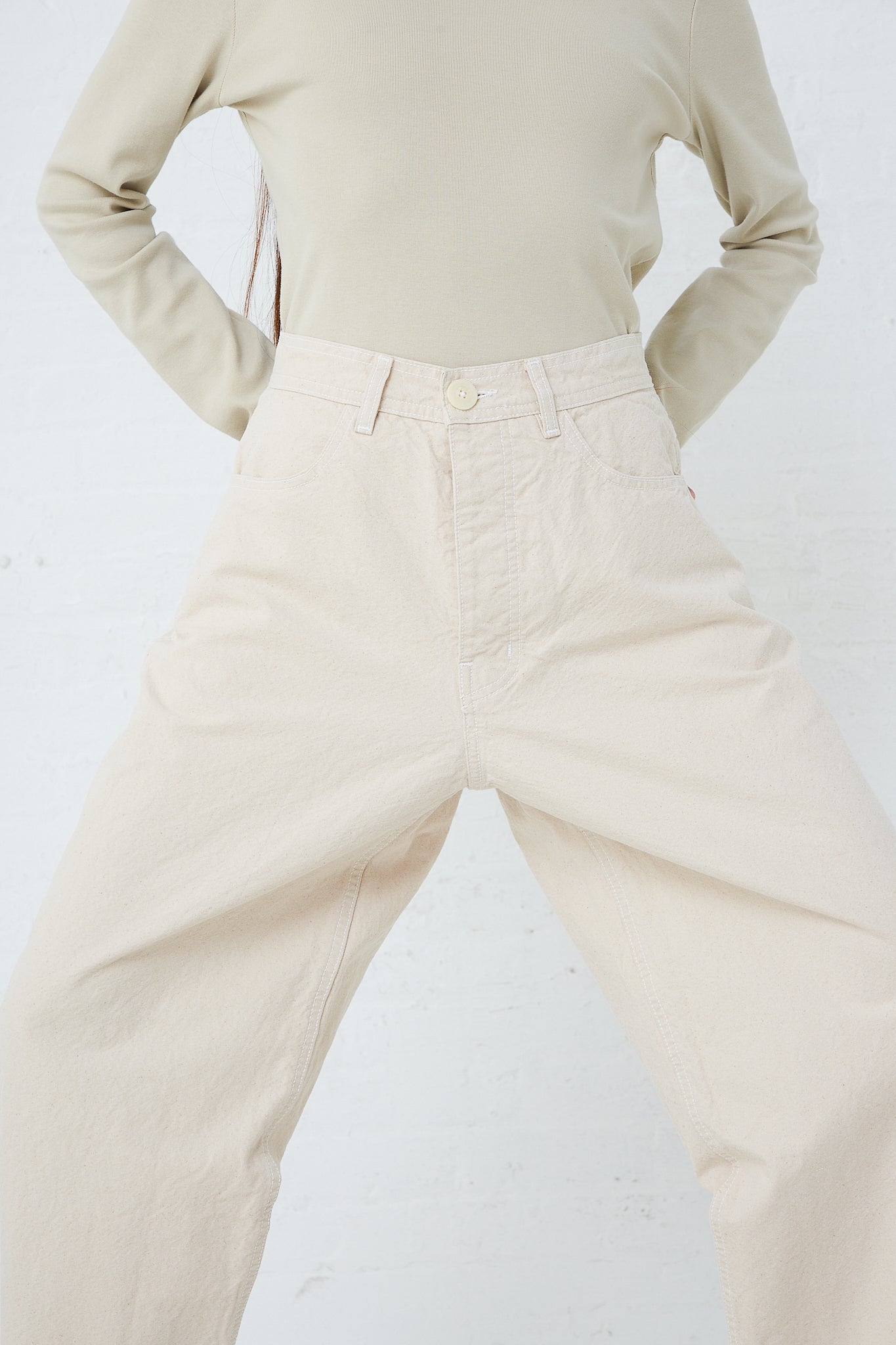 A woman in beige pants is posing in front of a white wall wearing Jesse Kamm's Organic Canvas California Wide pant in Natural, a relaxed fit unisex pant.