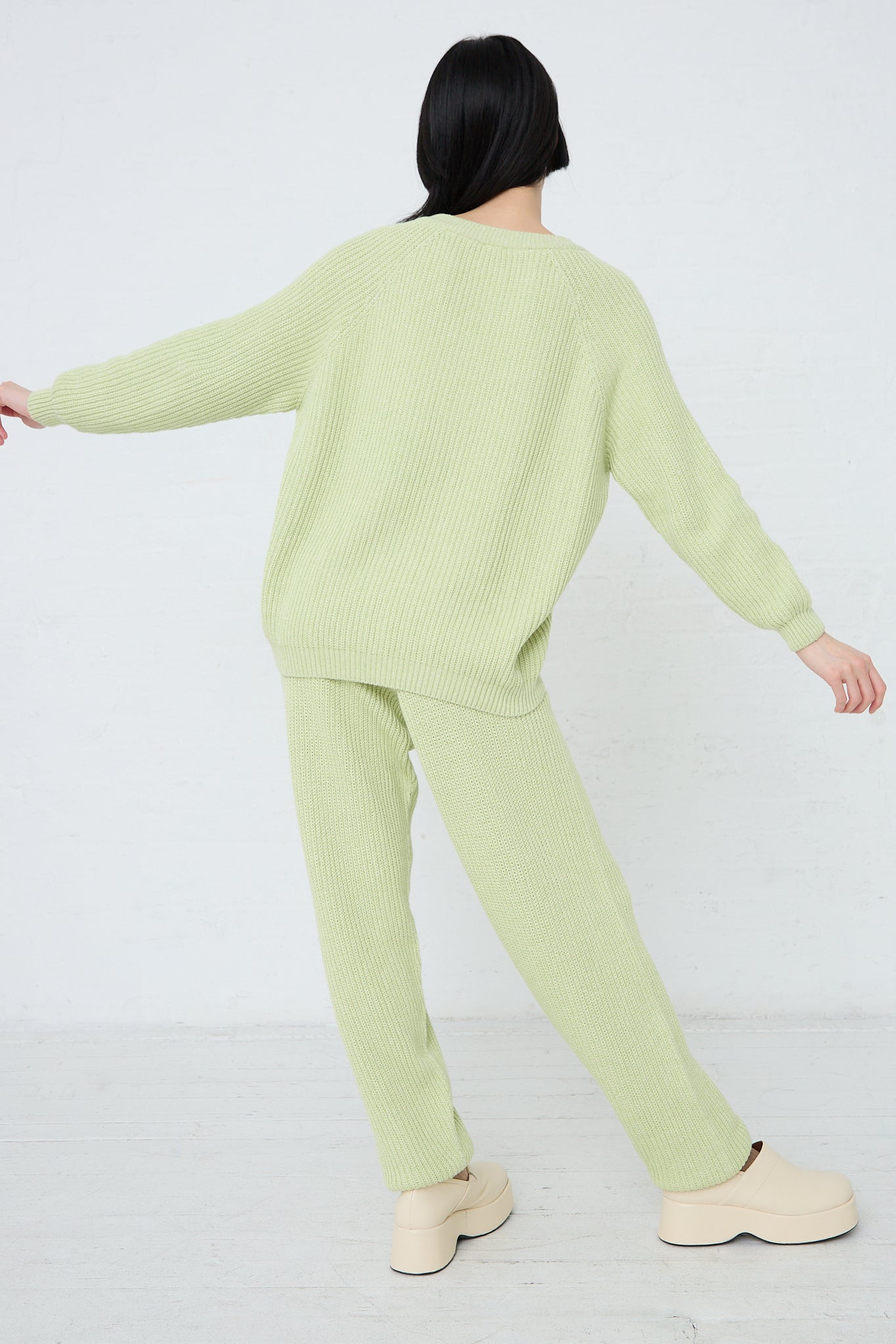 A woman wearing a green ribbed Baserange Cotton Dodd V Neck Pullover in Mimosa (Green). Back view.