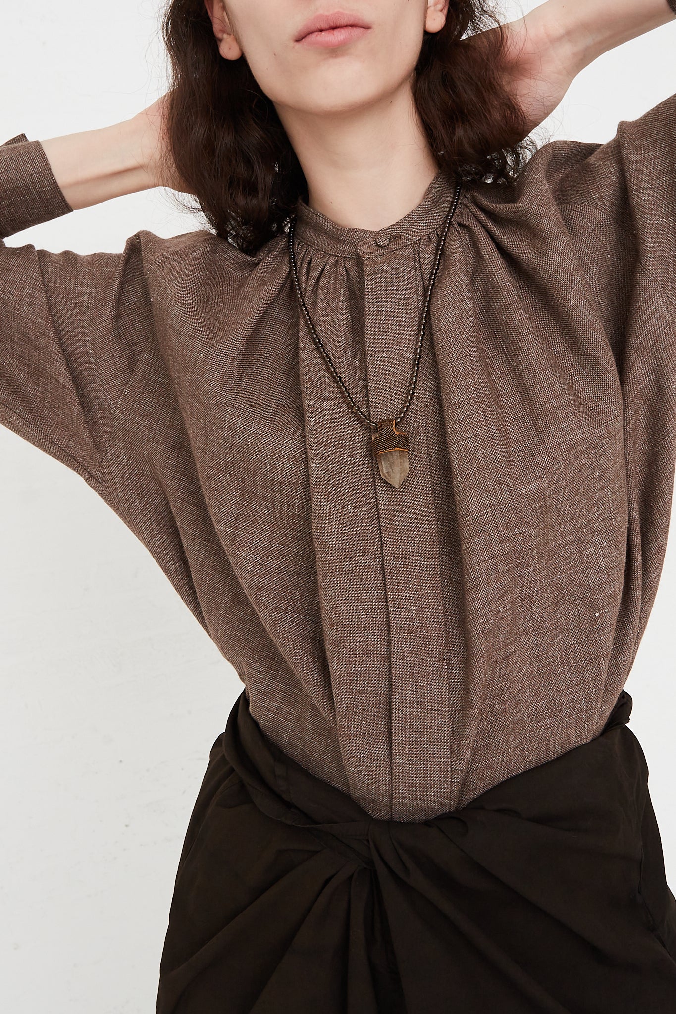 A woman wearing a brown shirt and black skirt adorned with the Robin Mollicone Long Pendulum Necklace in Smoky Quartz Beads Brown, Citrine Crystal.