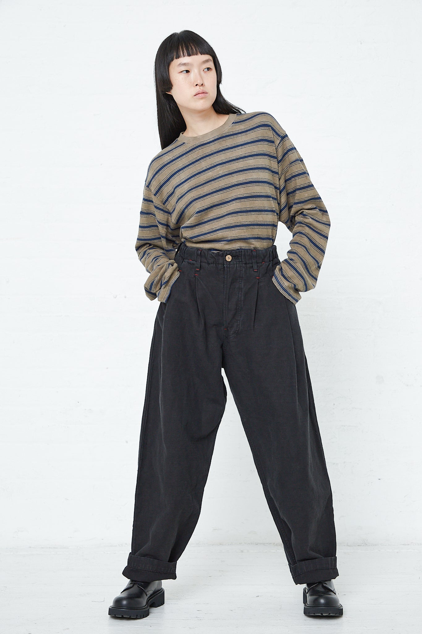 A woman wearing the Dr. Collectors 9 oz. Cotton and Hemp P40 Z Boys Military Pant in Sulfur Black with an elasticated waistband, paired with a striped sweater.