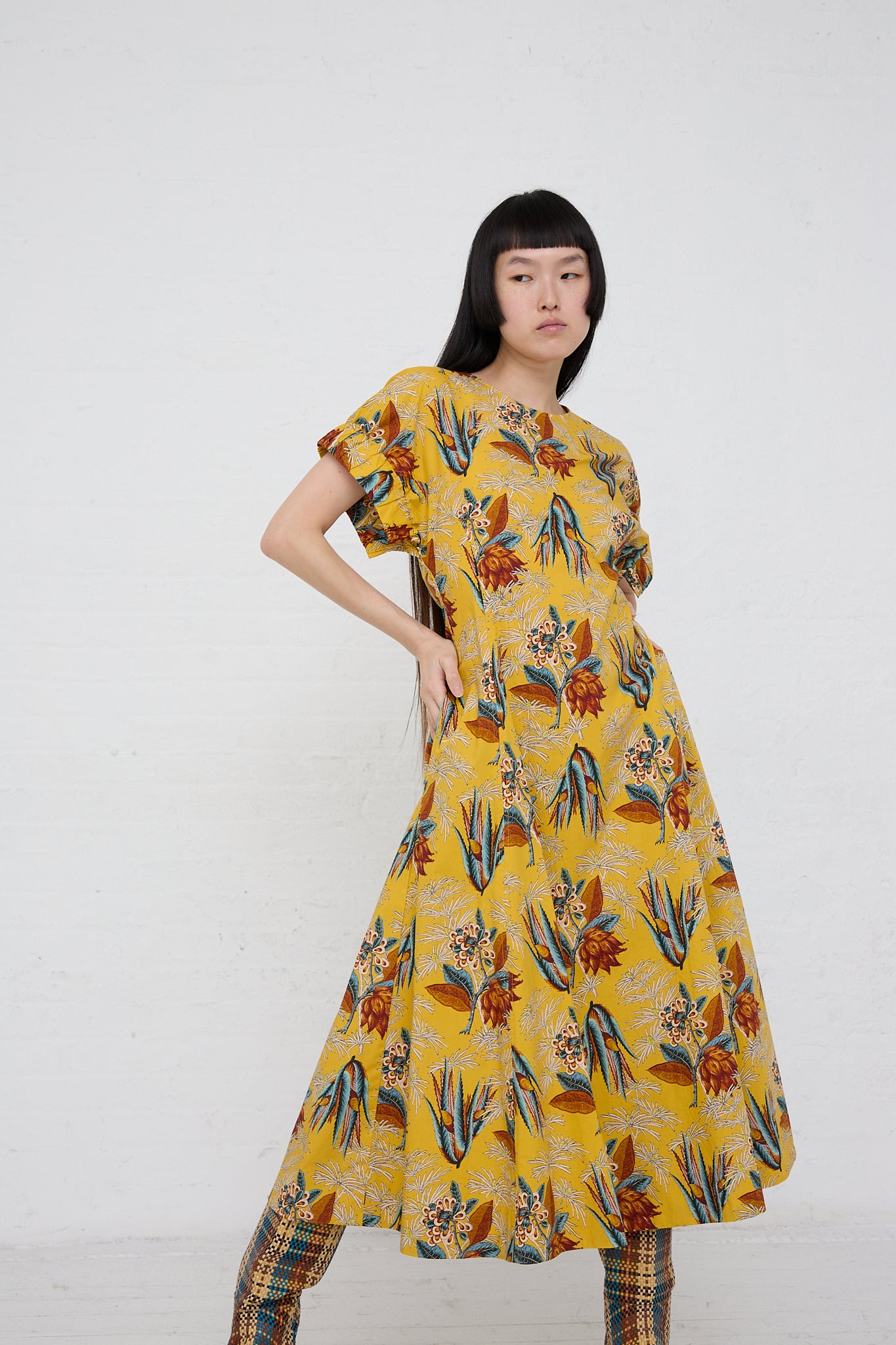 A woman in a Ulla Johnson Devon Dress in Marigold posing in front of a white wall.