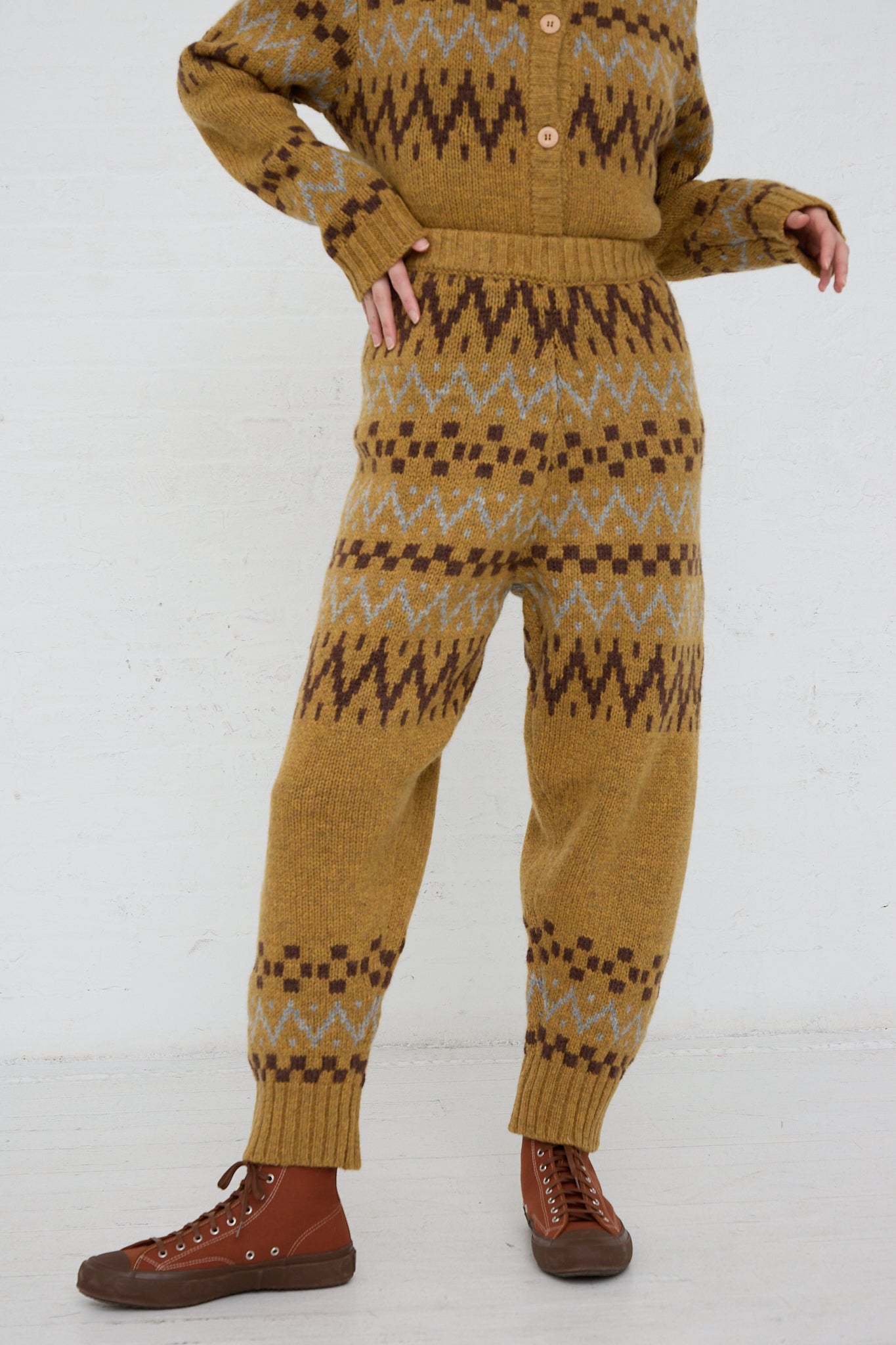 A woman is standing in an Ichi mustard sweater and jumpsuit, wearing an Ichi multi-color Knit Pant in Camel.