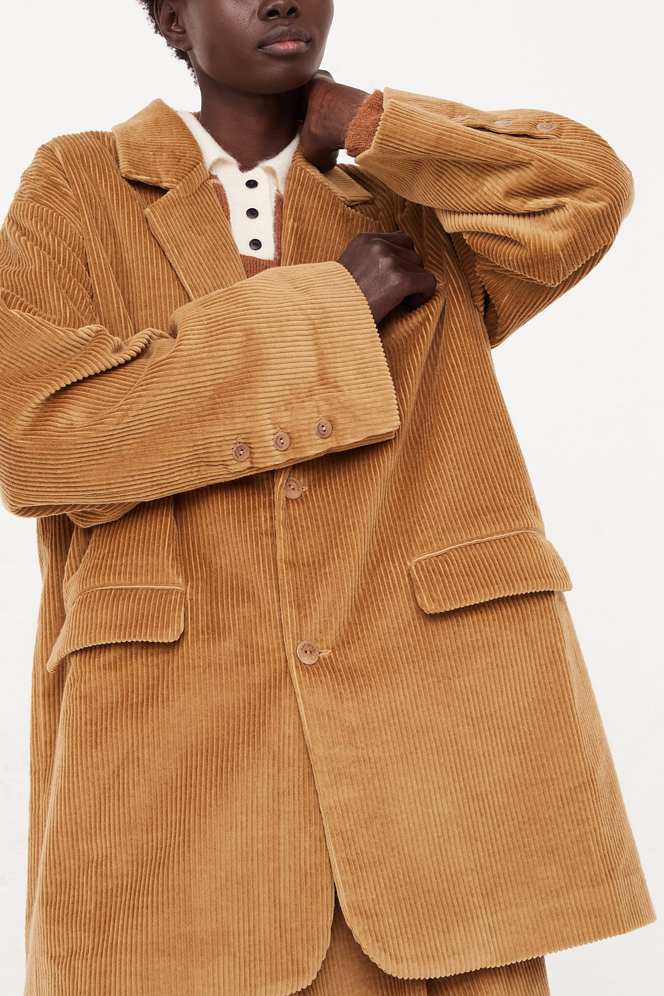 A model wearing a button blazer in a cotton corduroy featuring a notched collar, two flap pockets in front, and back vent. Blazer closed. Up close view of corduroy details. Oversized fit. Designed by Cordera - Oroboro Store