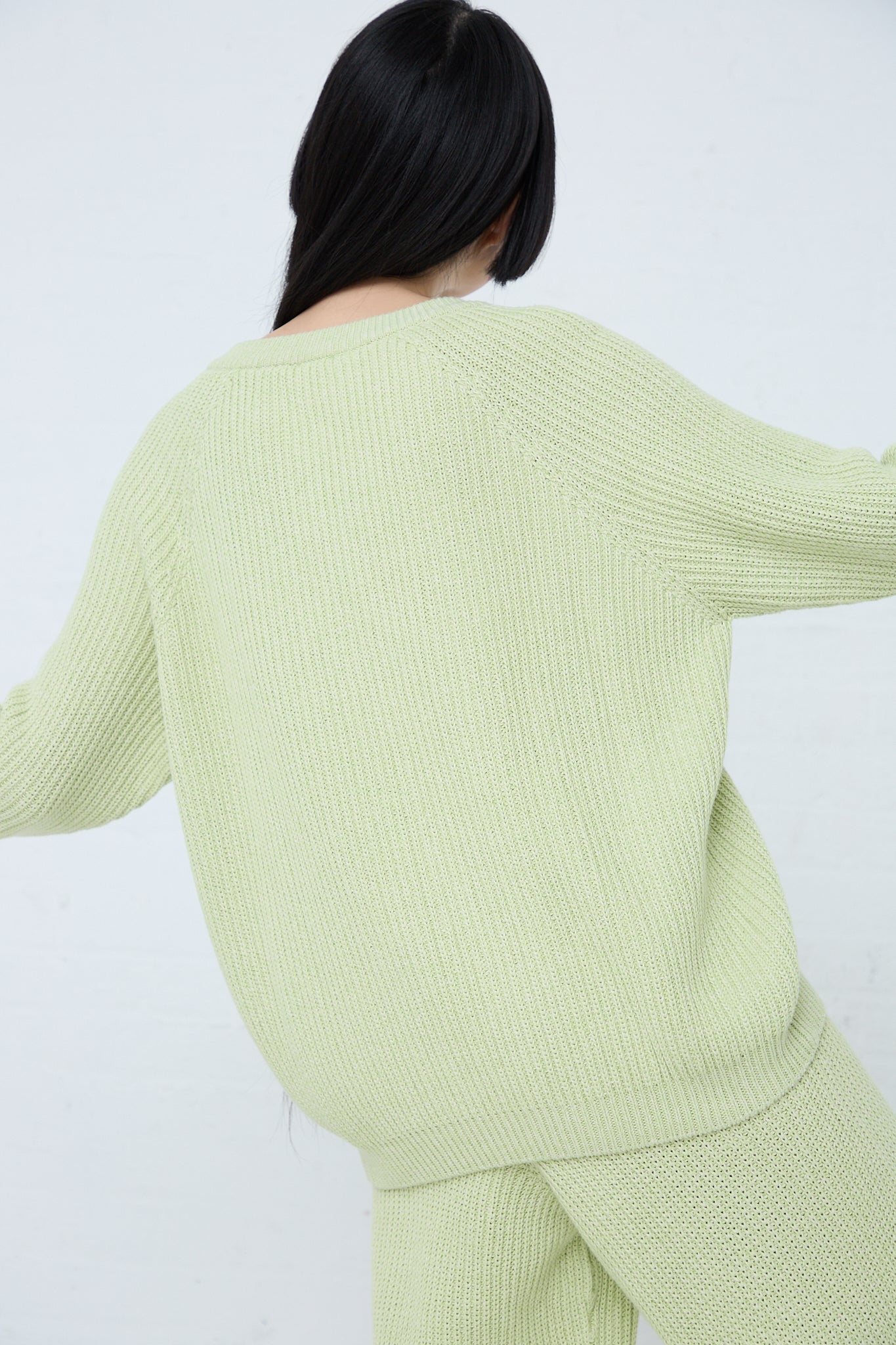 The back of a woman wearing a Baserange Cotton Dodd V Neck Pullover in Mimosa green sweater. Up close view.