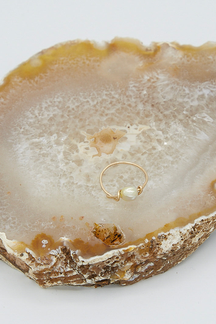A 14K Mermaid Ring in Golden Pearl by Mary MacGill sits on top of an agate slice.