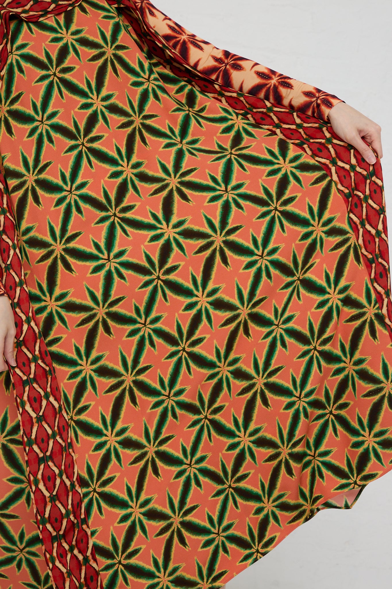 A woman wearing the Ulla Johnson Lily Dress in Fresco, an orange and green shibori printed midi dress. Up close view of fabric and details.