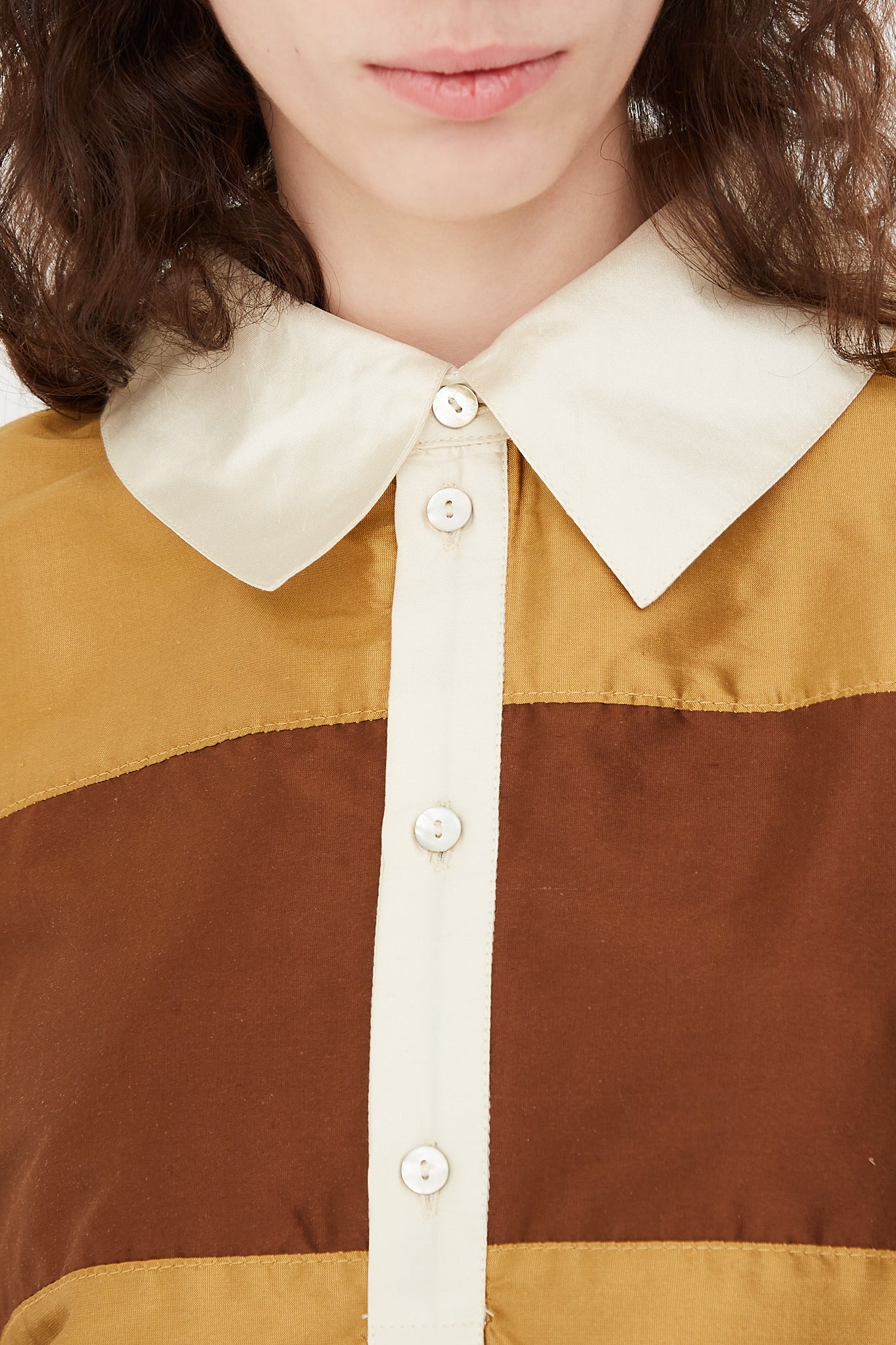 A model wearing a striped rugby shirt in a shiny silk doupion. Features a contrast fold-over collar and button placket, with an adjustable drawstring at hem. Front view and up close highlighting ivory collar details. Designed by Cawley - Oroboro Store 