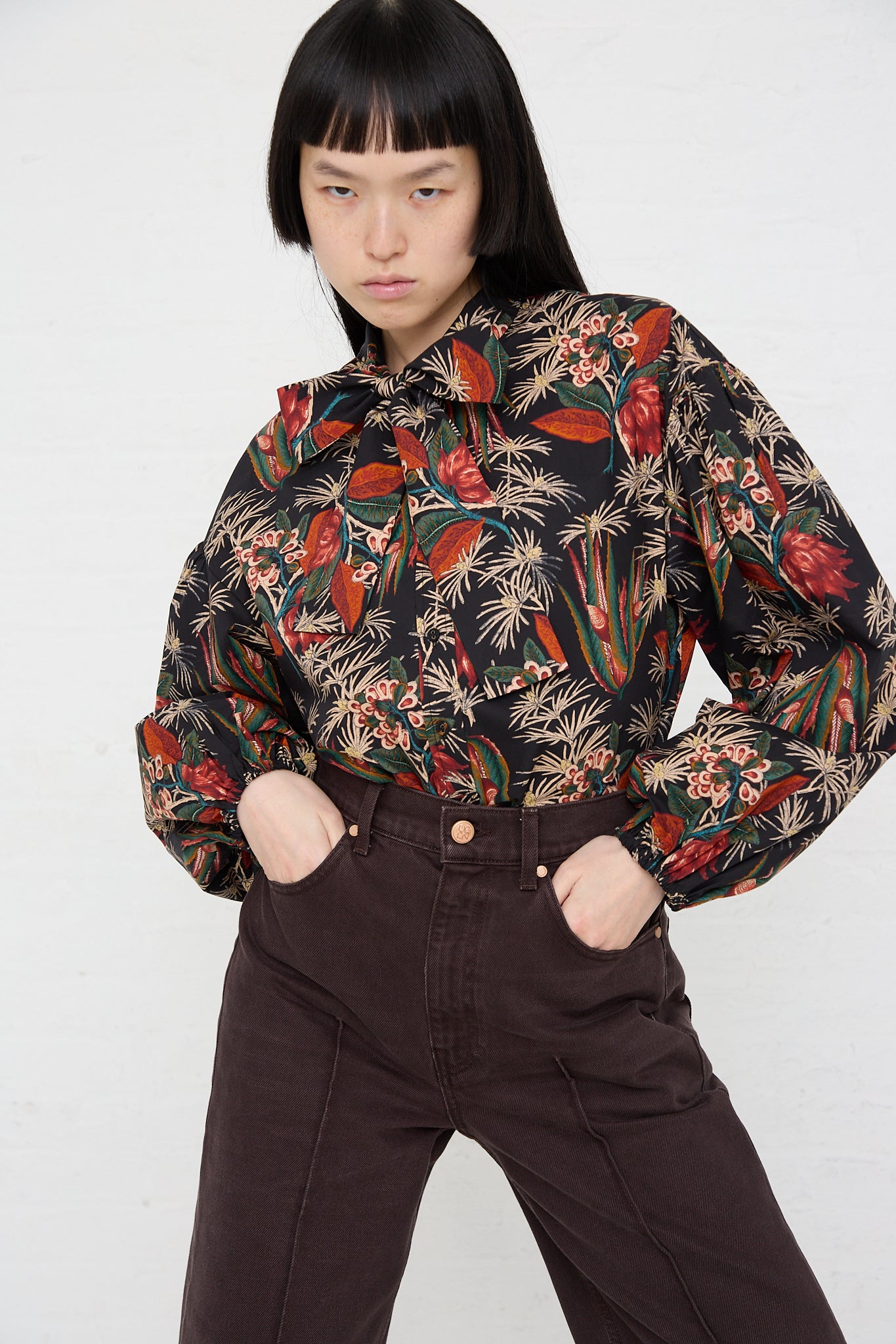 A woman wearing the Ulla Johnson Alberta Blouse in Anthurium. Front view. Model's hands are in front pockets.