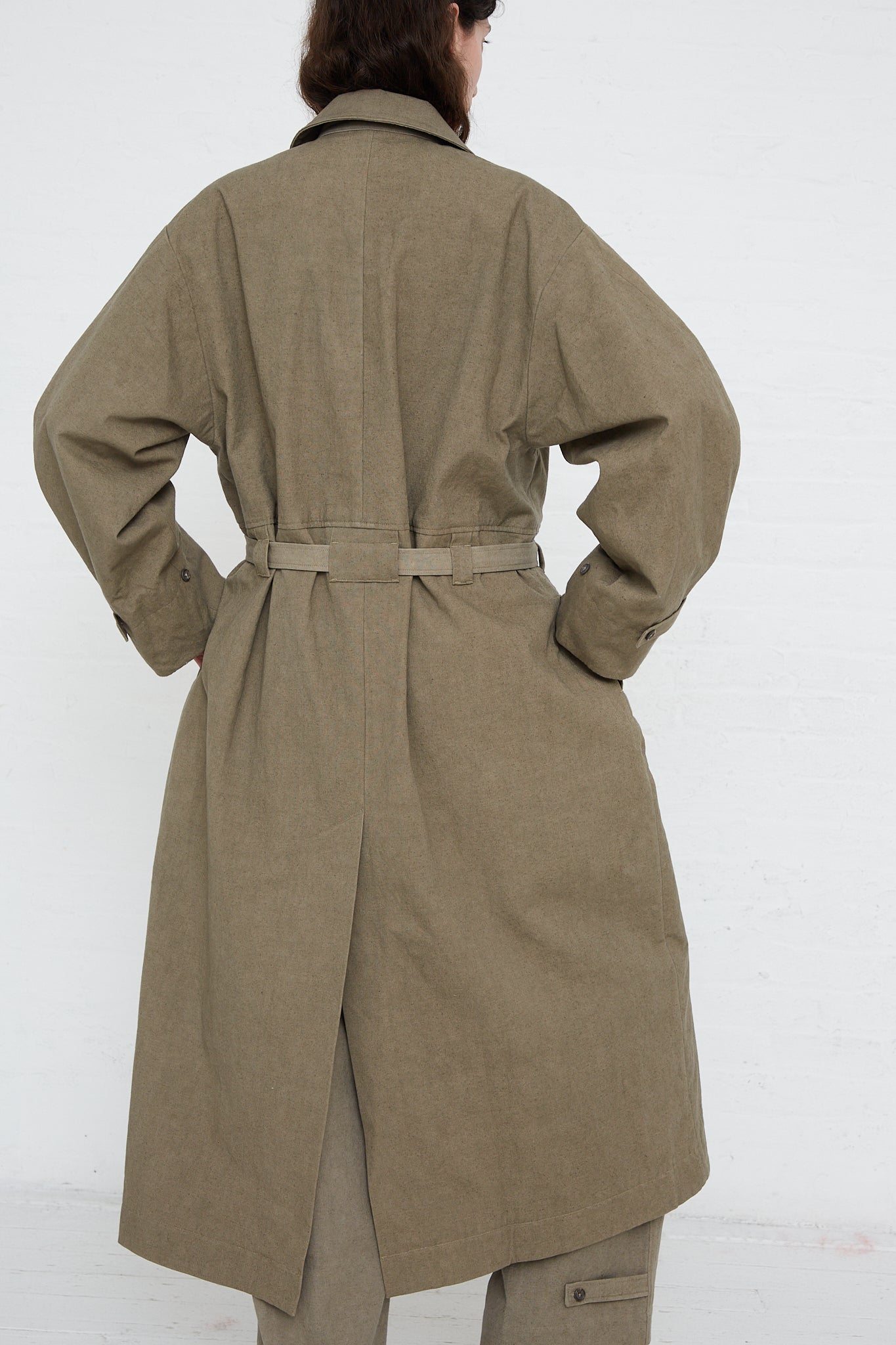 A woman wearing an oversized green Lauren Manoogian Belted Trench in Fatigue made of soft canvas with adjustable cuffs.