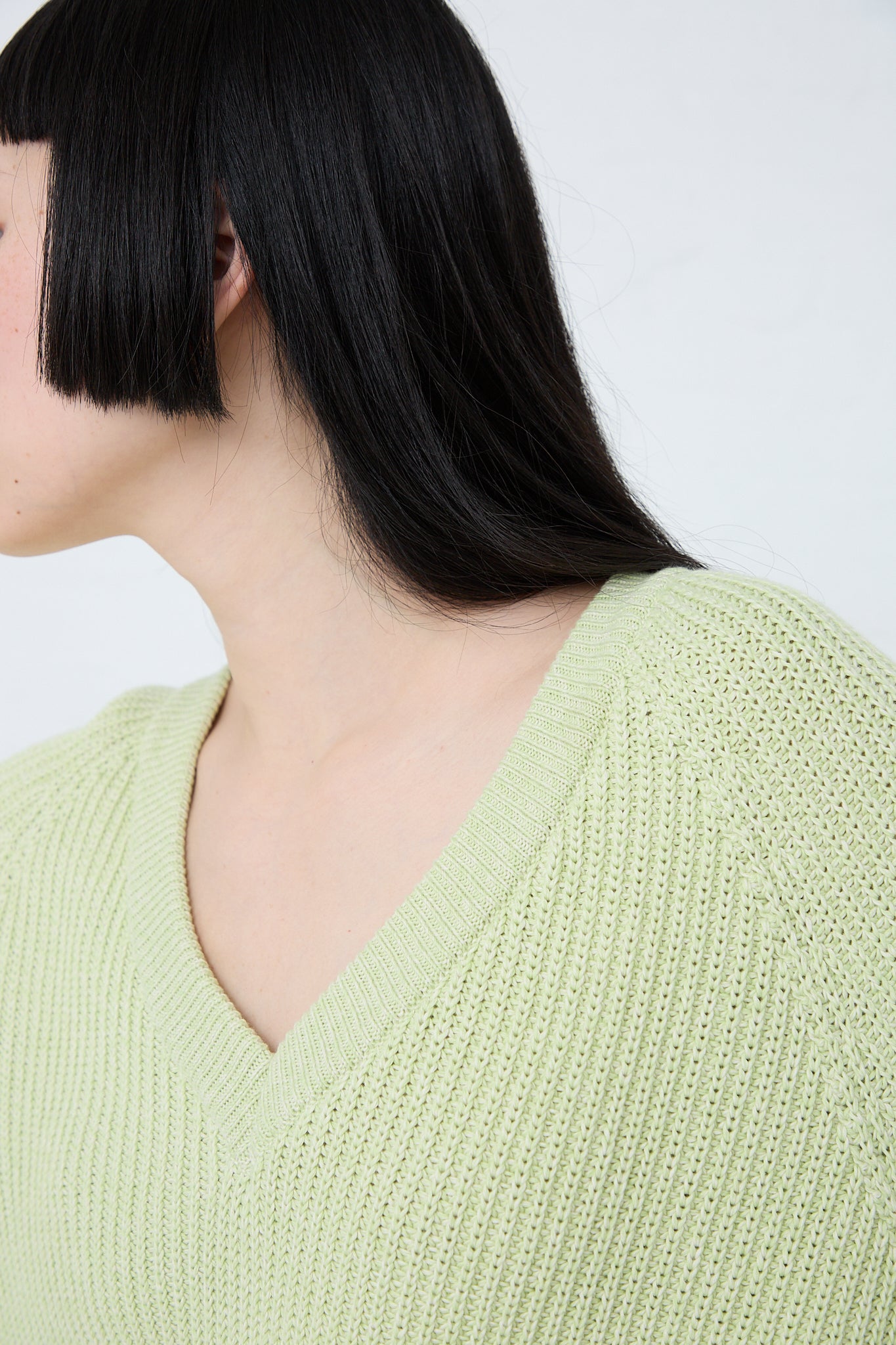A woman donning a long sleeve Cotton Dodd V Neck Pullover in Mimosa, by Baserange, featuring a slim-fit design and a captivating green v-neck sweater. Up close view.