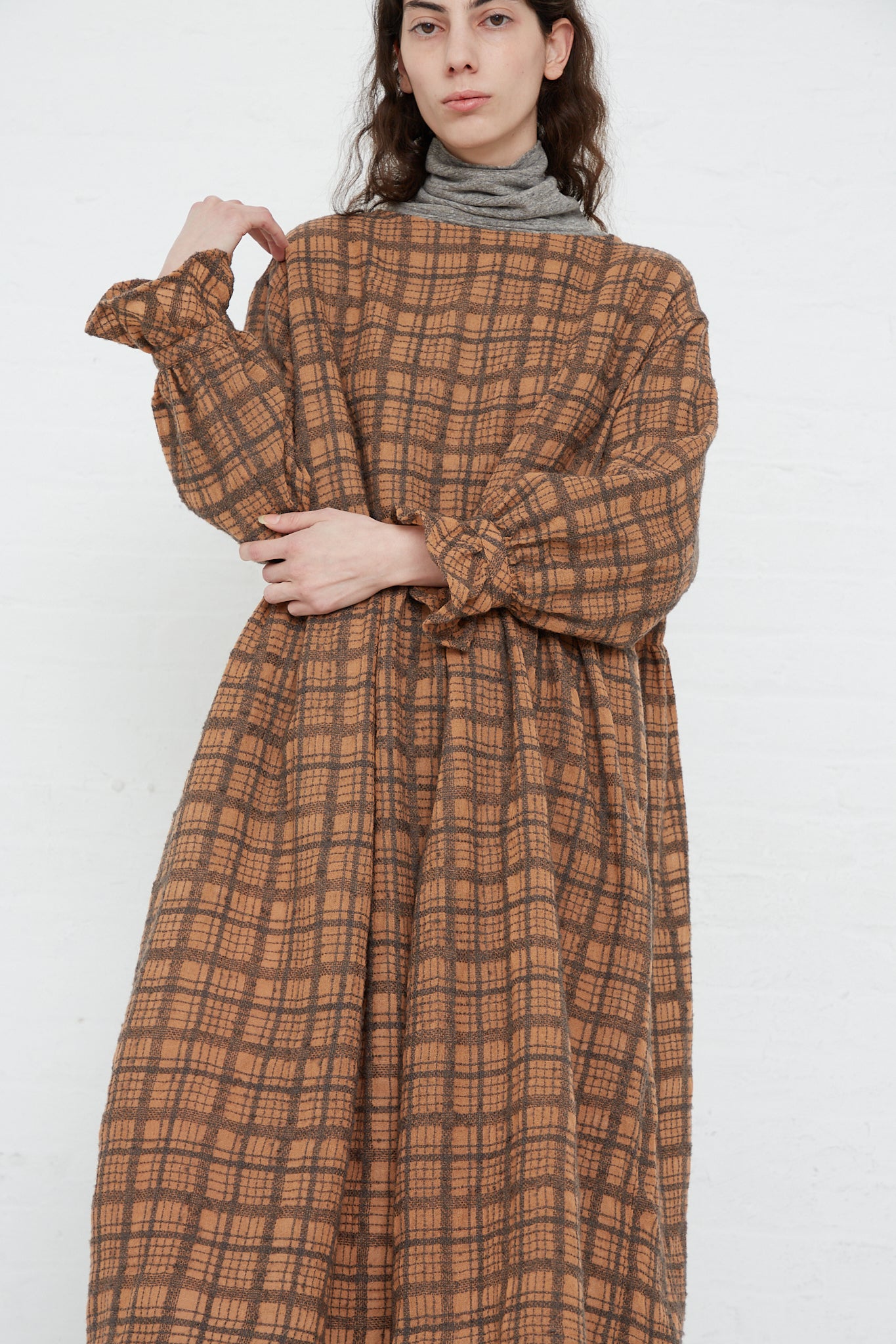 A woman wearing an Ichi Antiquités Woven Wool Check Dress in Terracotta, consisting of a wide neck and long sleeves.