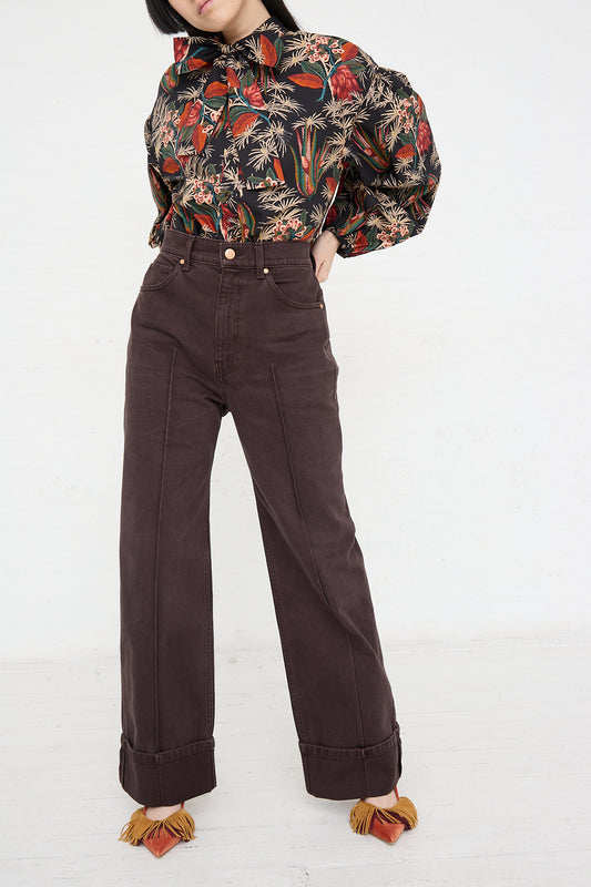 A woman wearing a floral blouse and brown wide leg pants by Ulla Johnson in Los Angeles. The pants she is wearing are The Genevieve Jean in Mahogany Wash.