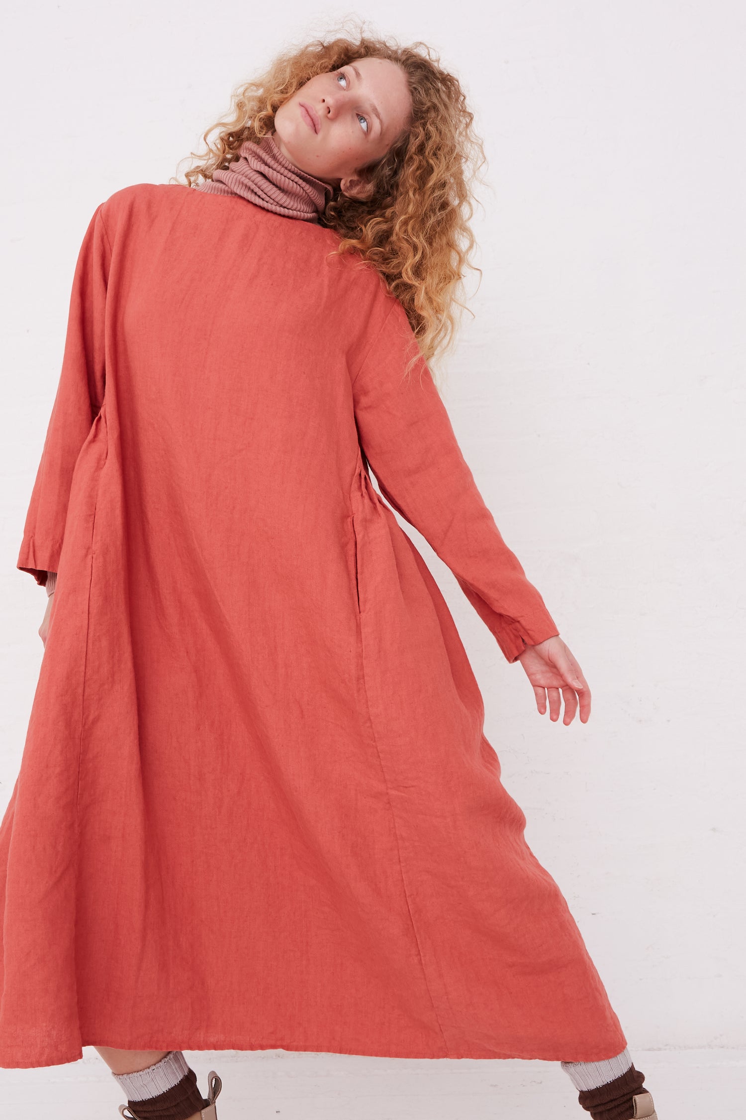A model in a Kortrijk Linen Dress in Pink by Ichi Antiquités is posing in front of a white wall.