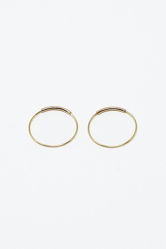 A pair of Kathleen Whitaker Hoop Earrings Extra Small 5/8" Pair Earrings in 14K Yellow Gold on a white surface.