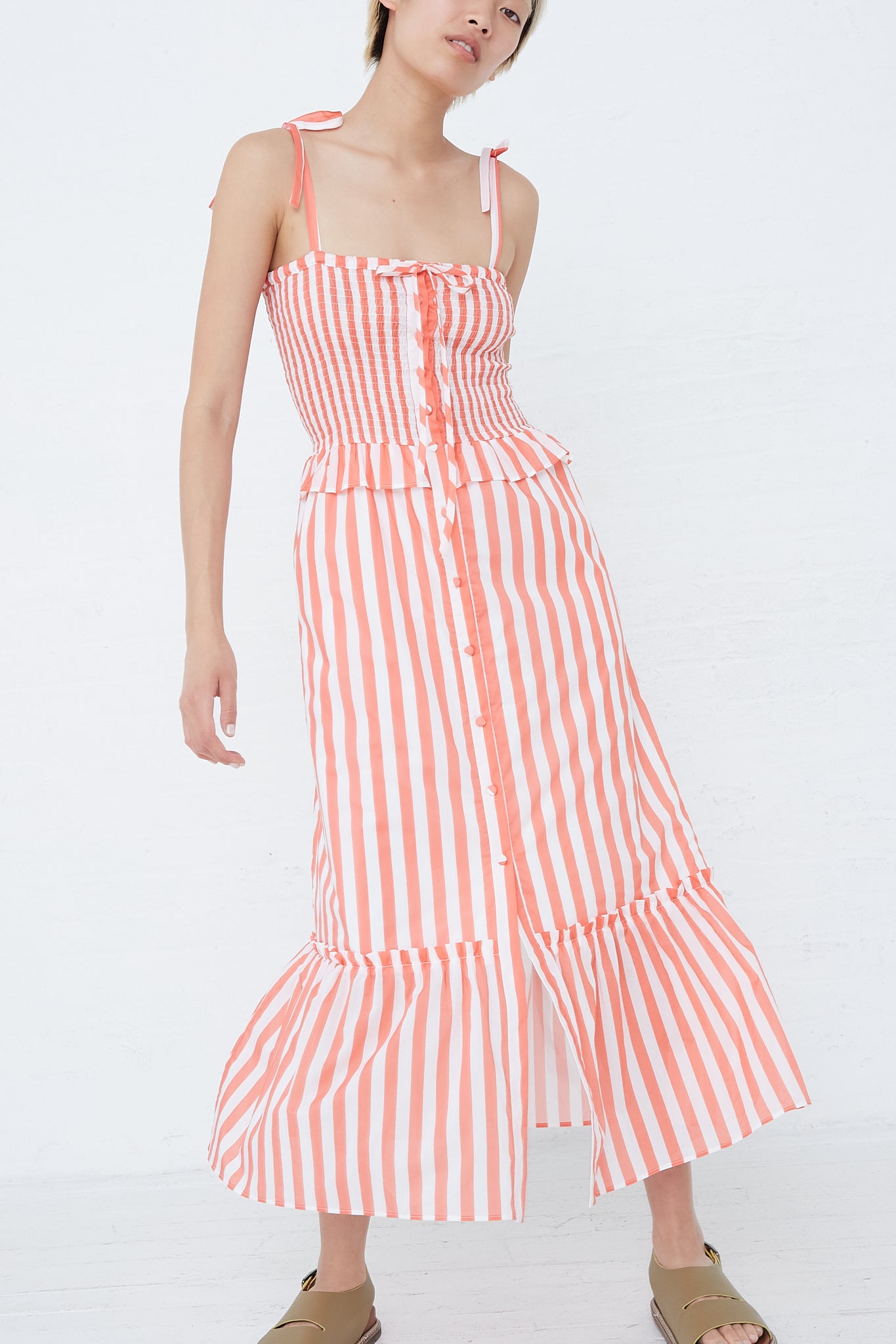 The model is wearing the Loretta Caponi Alberica Dress in Coral Stripe, an orange and white striped midi dress with adjustable tie straps.
