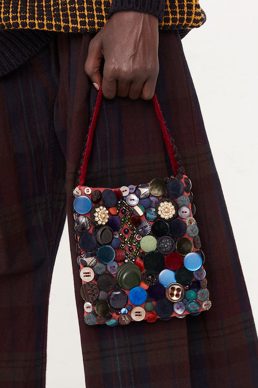 A model is holding an Intensity Beaded Bag in Velvet with buttons.