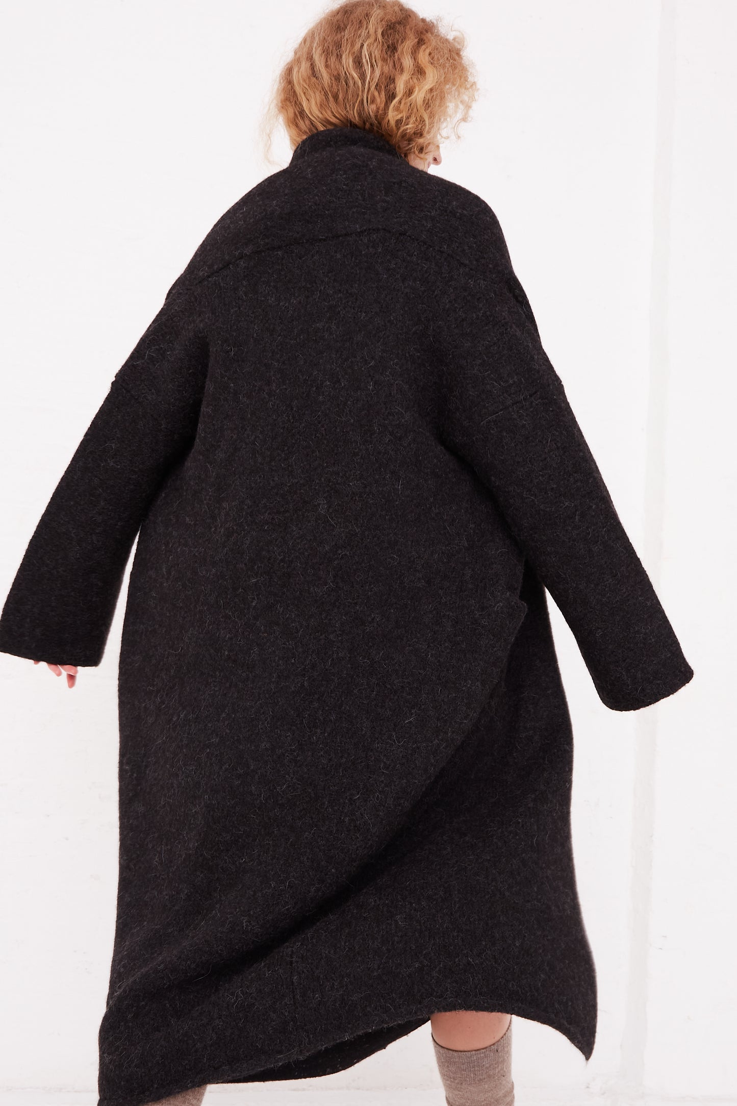A woman is walking in a Lauren Manoogian Long Shawl Cardigan in Black made of Alpaca blend knit.