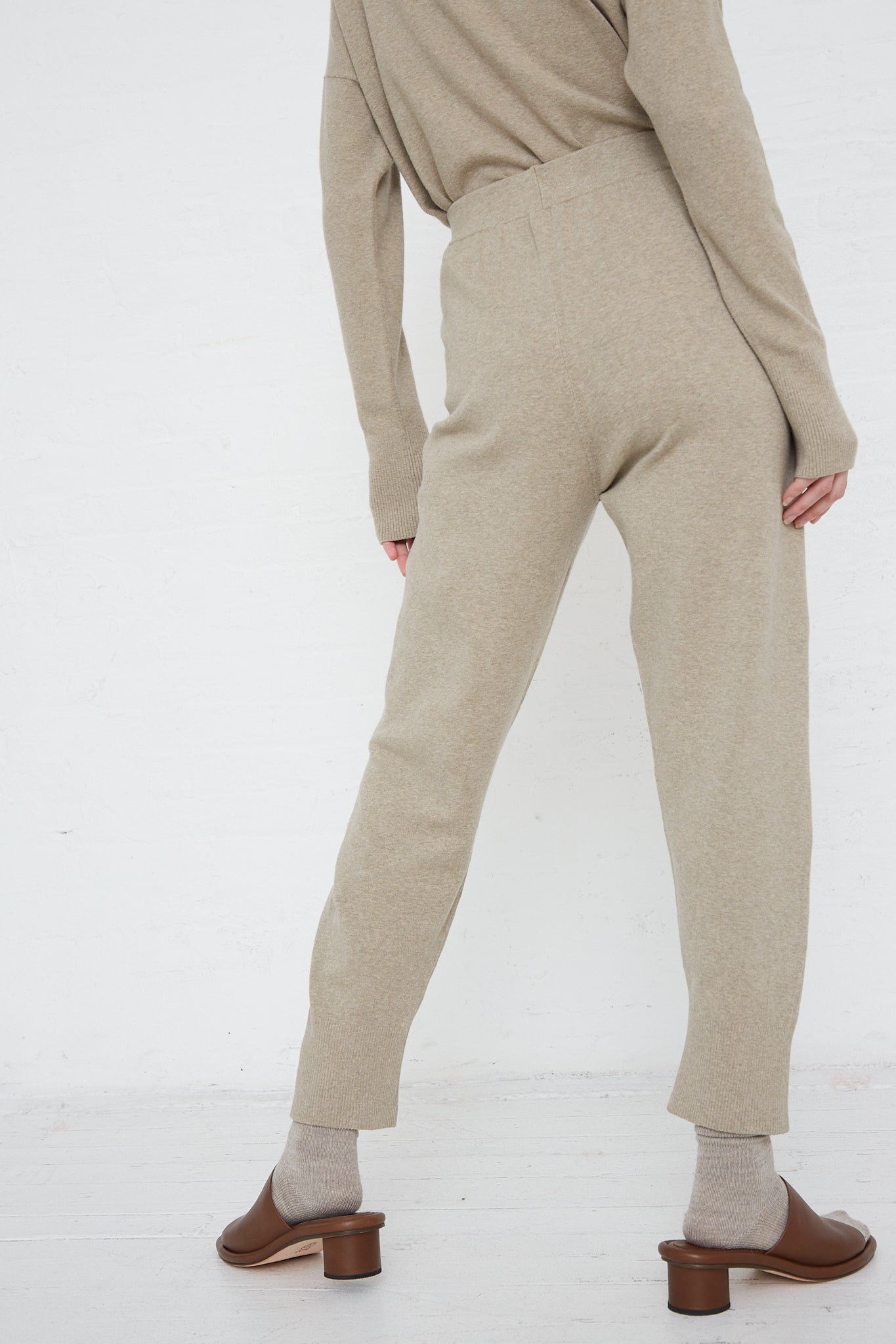 The back view of a woman wearing Lauren Manoogian's Base Pant in Stone Melange beige sweater and relaxed fit pants with an elasticated waist.