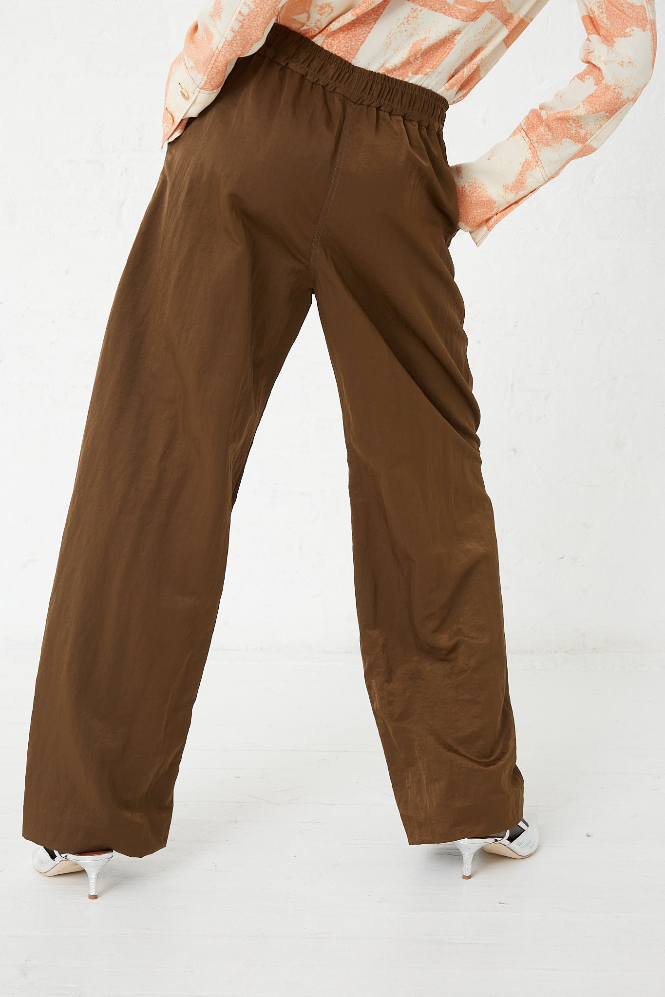 A woman is standing in a pair of Rejina Pyo's Nylon Una Trousers in Brown with an elasticated waist.