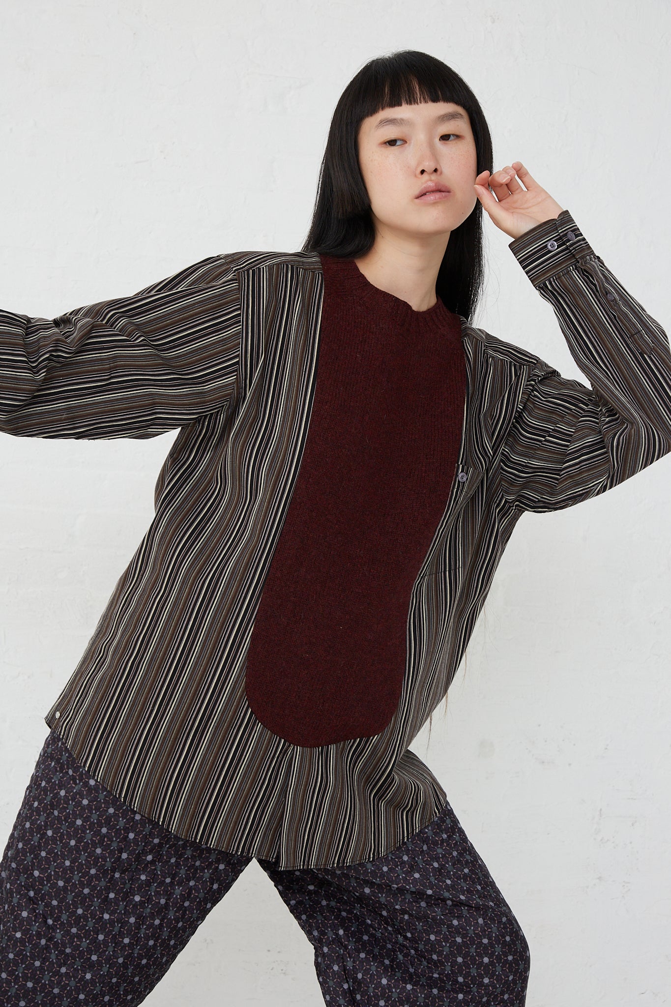 A woman wearing a long sleeve No. 68 Front Insert Pullover in Stripe from the brand Bless, in a striped shirt and pants, made of a wool and cotton blend.