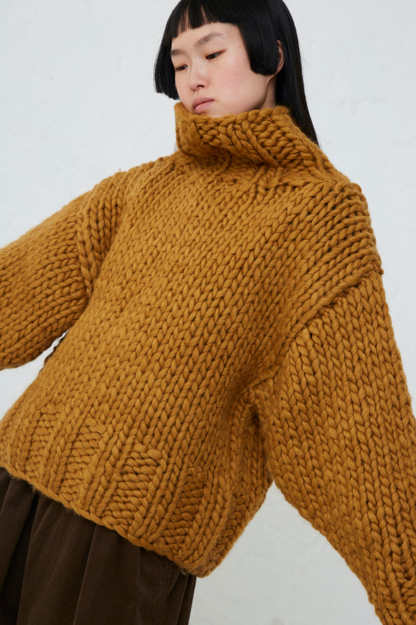 The model is wearing an Ichi wool hand-knit pullover in mustard.