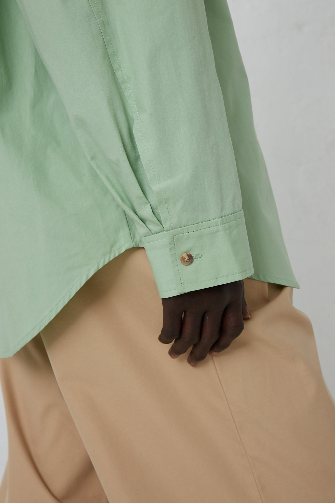 A woman wearing a Rejina Pyo Organic Cotton Caprice Shirt in Mint with a front button closure and tan pants.