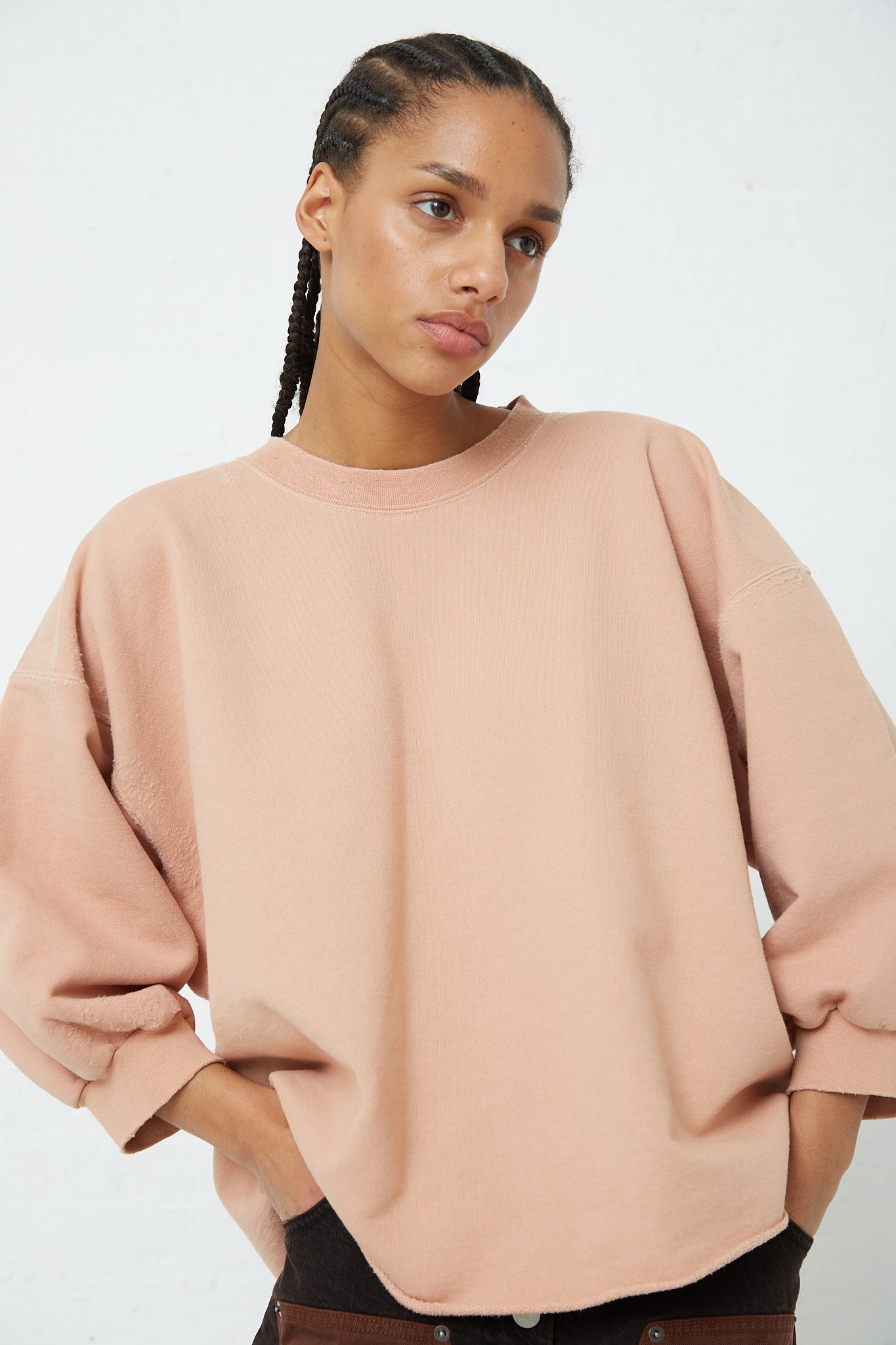 The model is wearing a Fond Sweatshirt in Fawn by Rachel Comey, which is a distressed cotton blend pink sweatshirt with a raw edge hemline.