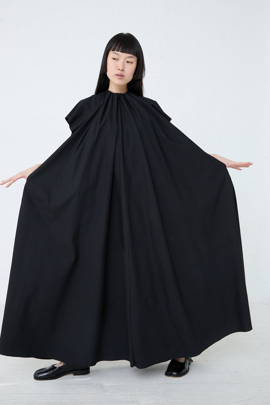 A woman in an oversized fit black MM6 cotton poplin maxi dress with her arms outstretched.