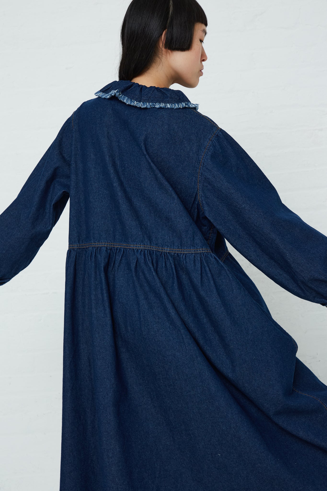 A woman is wearing an Ichi Cotton Collar Dress in Dark Indigo with a ruffled hem and long sleeves.