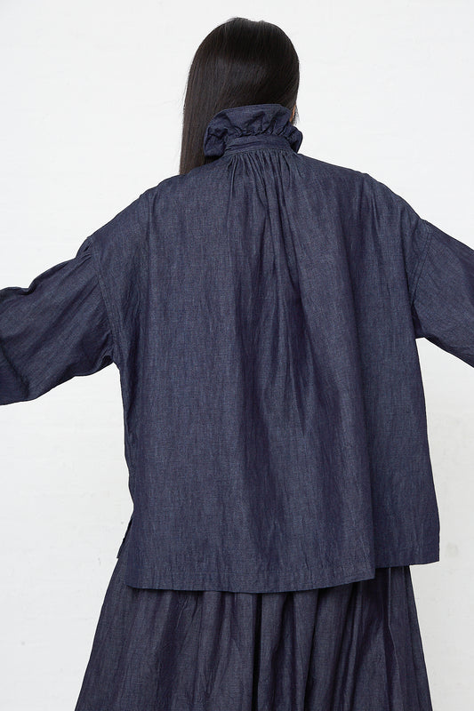 The back of a woman wearing a Toujours Cotton Denim Cloth Ruffle Shirt in Indigo jacket.