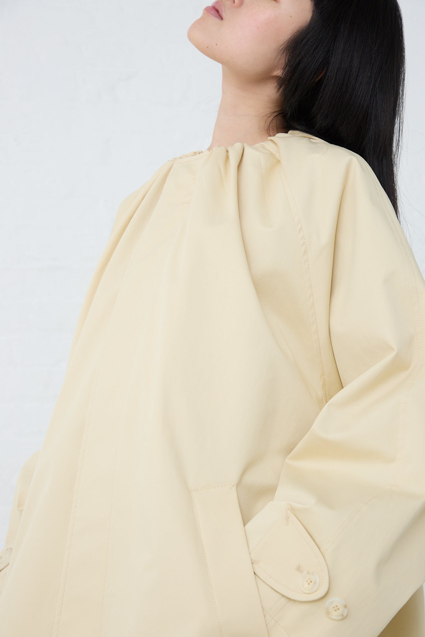 A woman wearing a MM6 Pale Yellow Trench Coat. Side view and up close.