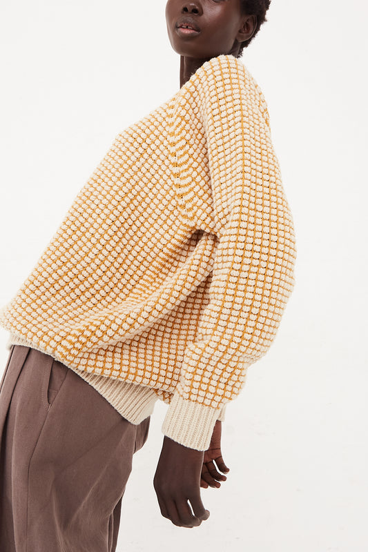 A woman donning an oversized yellow and brown checkered Crewneck Sweater in Natural Gold Lalin made of merino wool by Jan-Jan Van Essche.