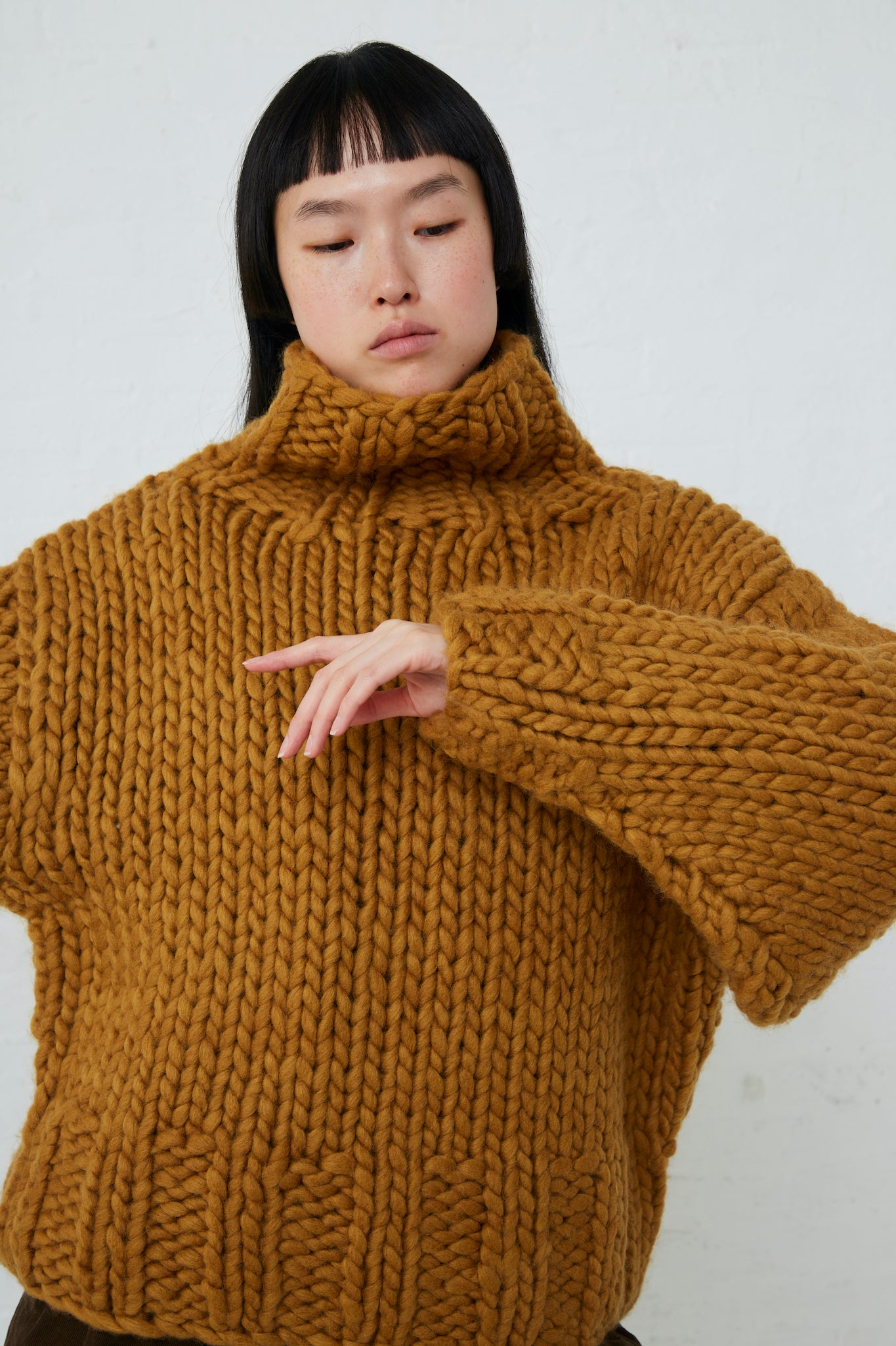 A woman wearing a Ichi Wool Hand-Knit Pullover in Mustard turtleneck sweater.