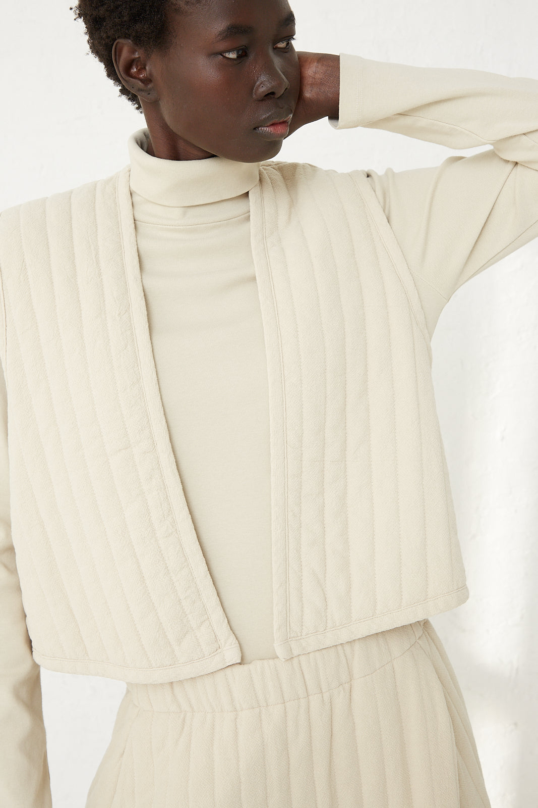 The model is wearing a cream turtleneck and quilted pants from an open Quilted Vest in Ivory, Black Crane.