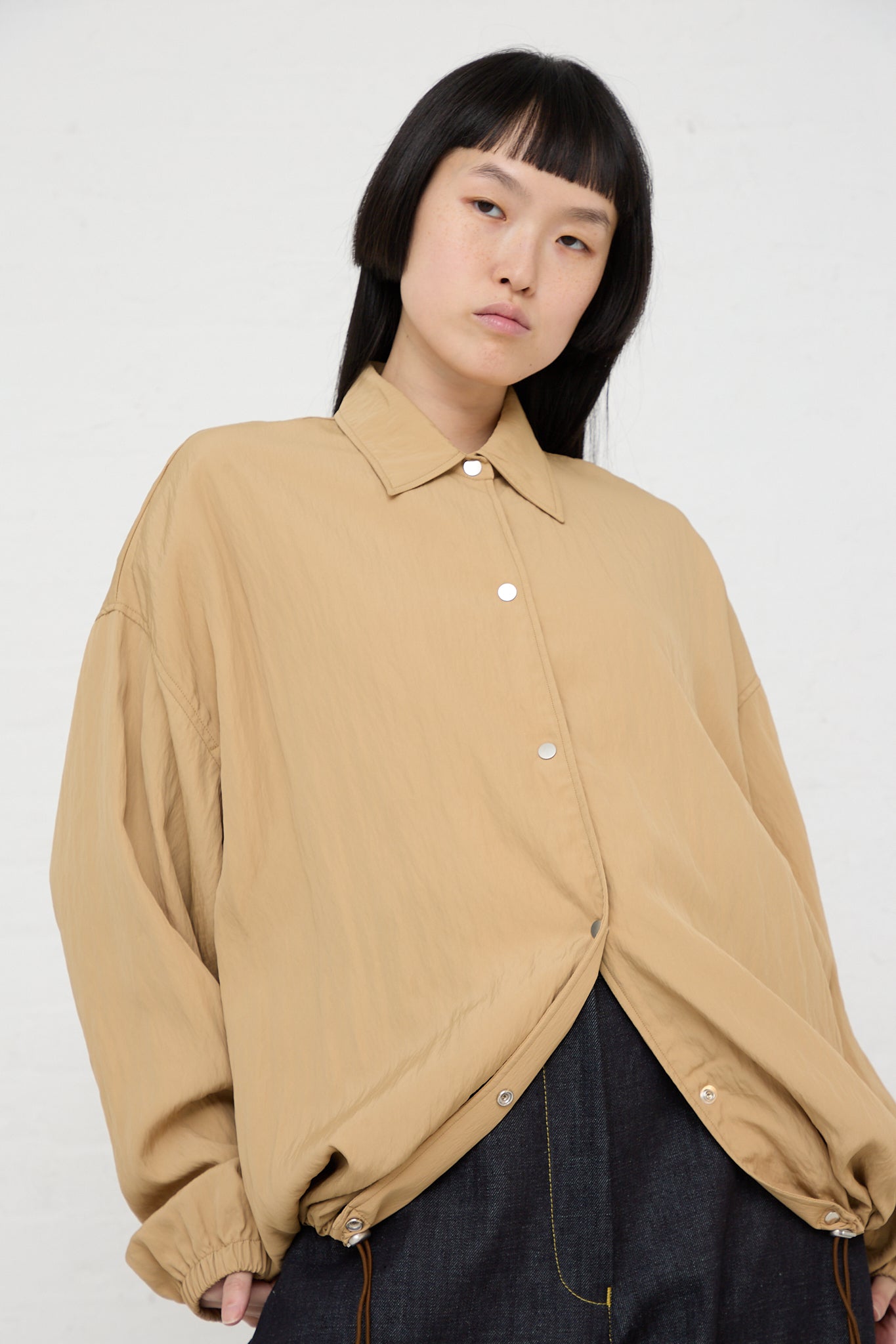 A woman wearing a Sprung Coach Jacket in Sand by Studio Nicholson made of a viscose blend fabric.