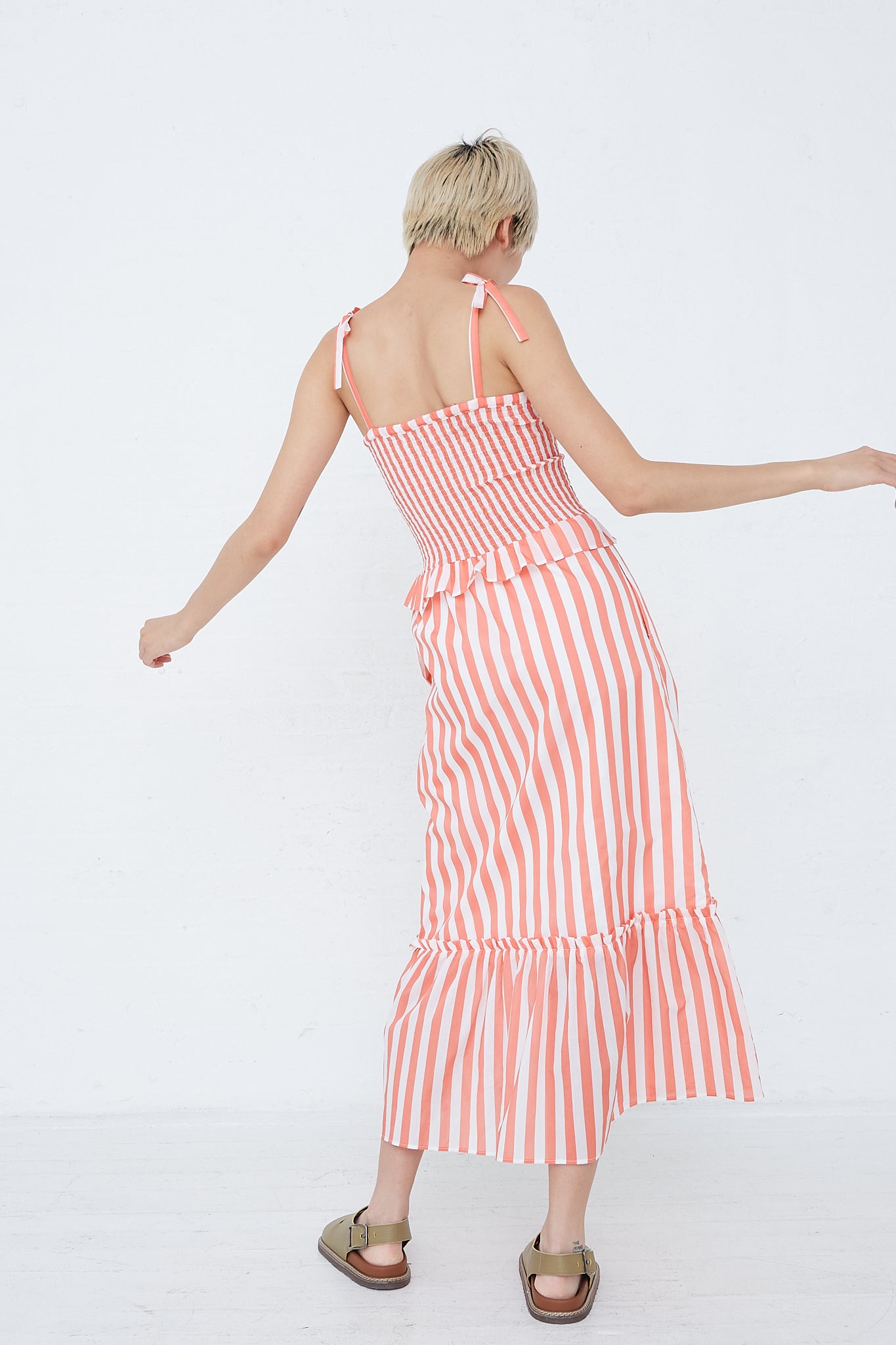 A woman in an Alberica Dress in Coral Stripe by Loretta Caponi, with adjustable tie straps in striped cotton.