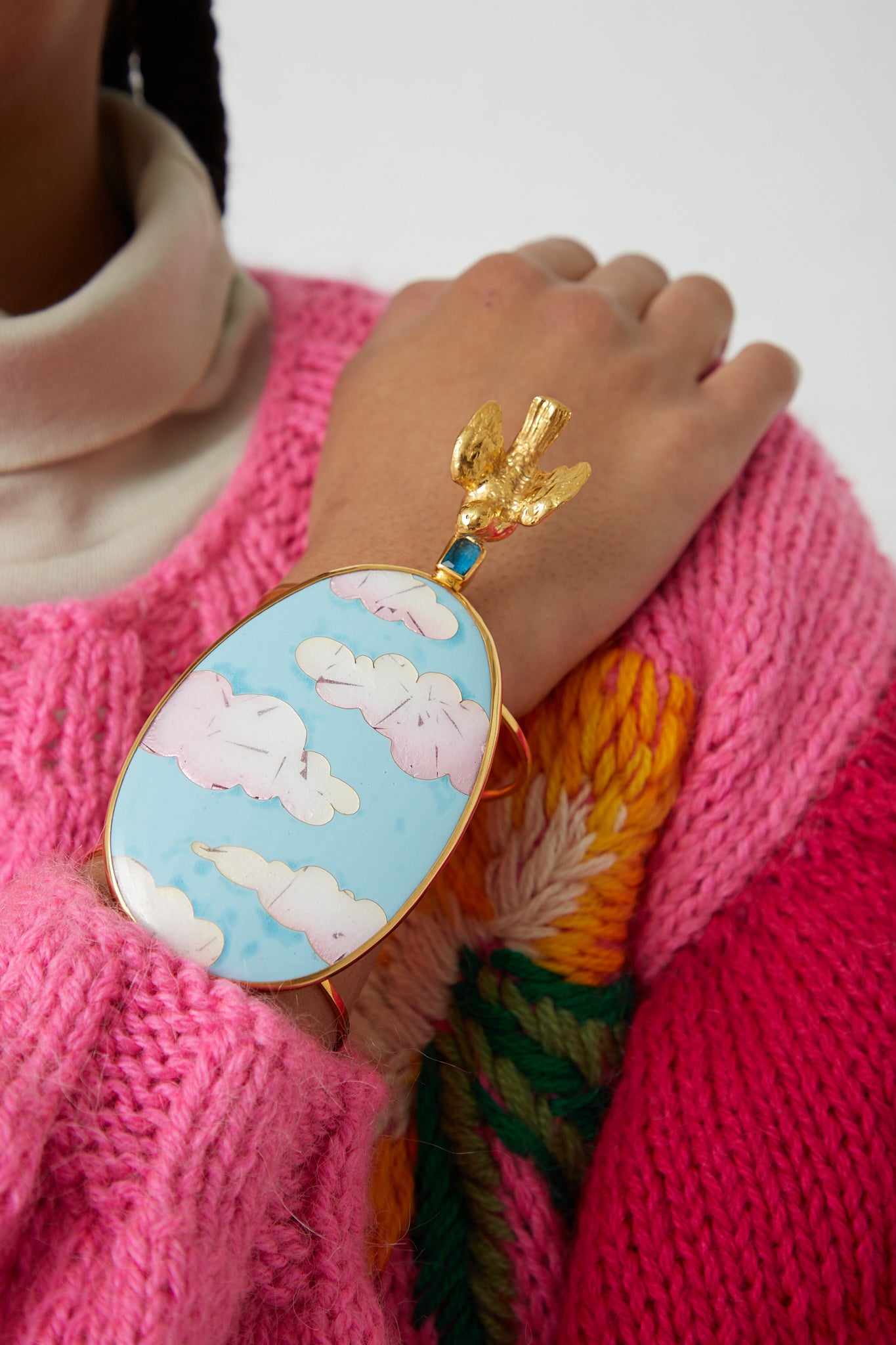 A woman wearing a pink sweater with a blue and white cuff adorned with a Sofio Gongli Bracelet in Clouds with Bird.