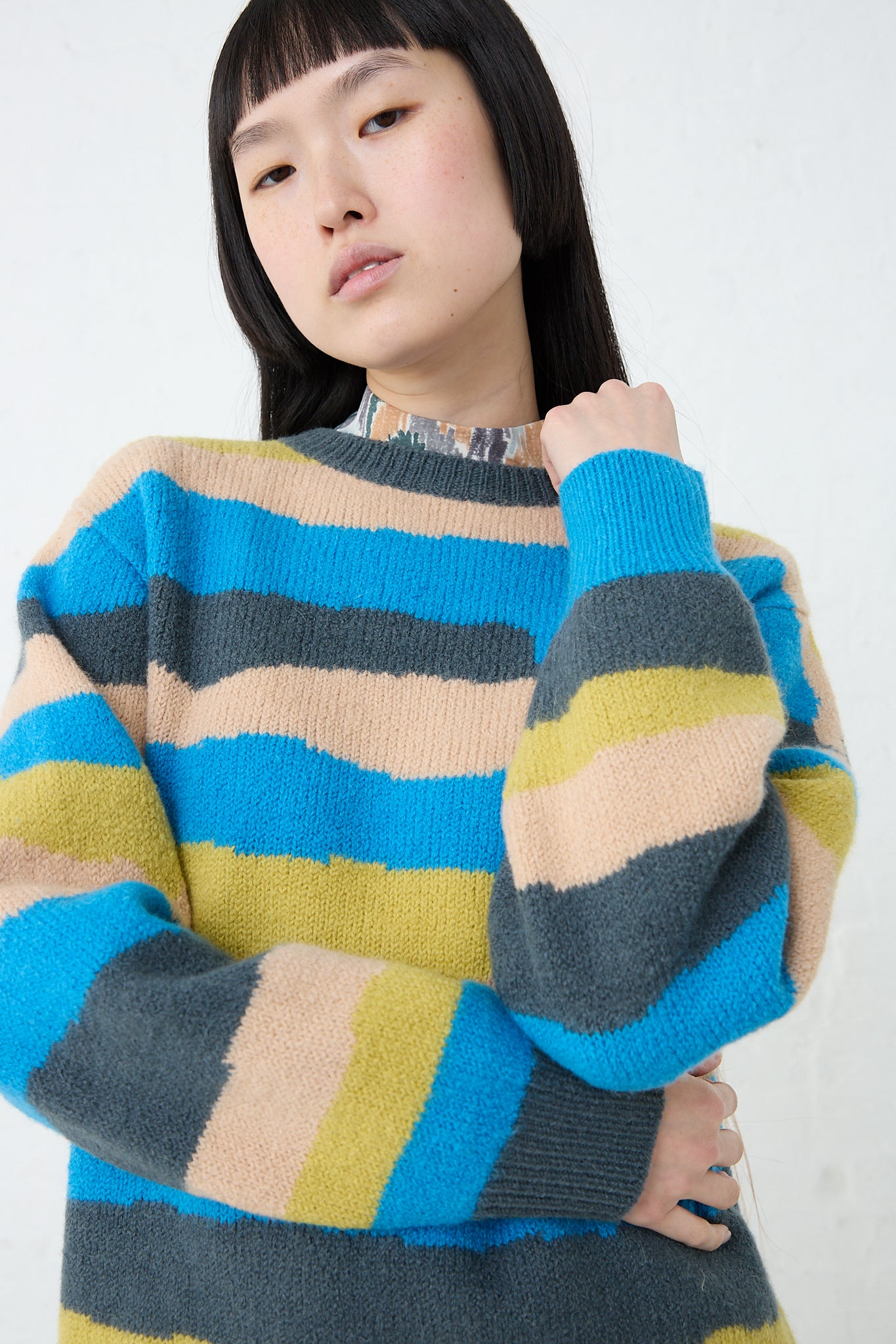 A woman wearing a Light Wind Sweater in Blue Mix, a Mina Perhonen striped sweater made of alpaca/wool blend.