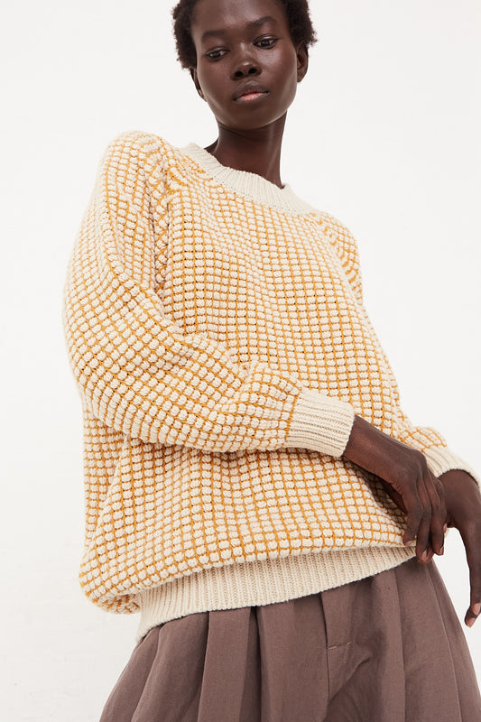 A model wearing an oversized yellow checkered Crewneck Sweater in Natural Gold Lalin and a tan skirt by Jan-Jan Van Essche.