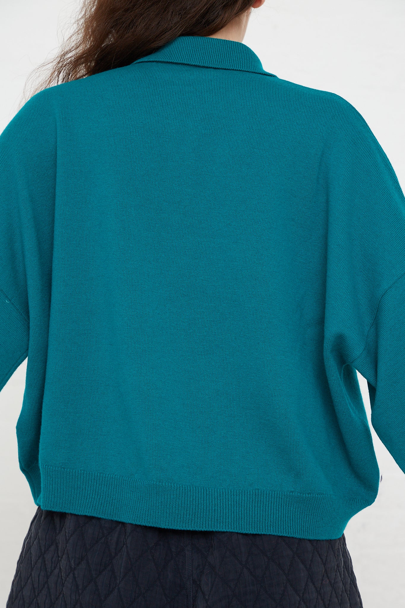 The back view of a woman wearing a Cordera Merino Wool Polo Sweater in Teal Green.