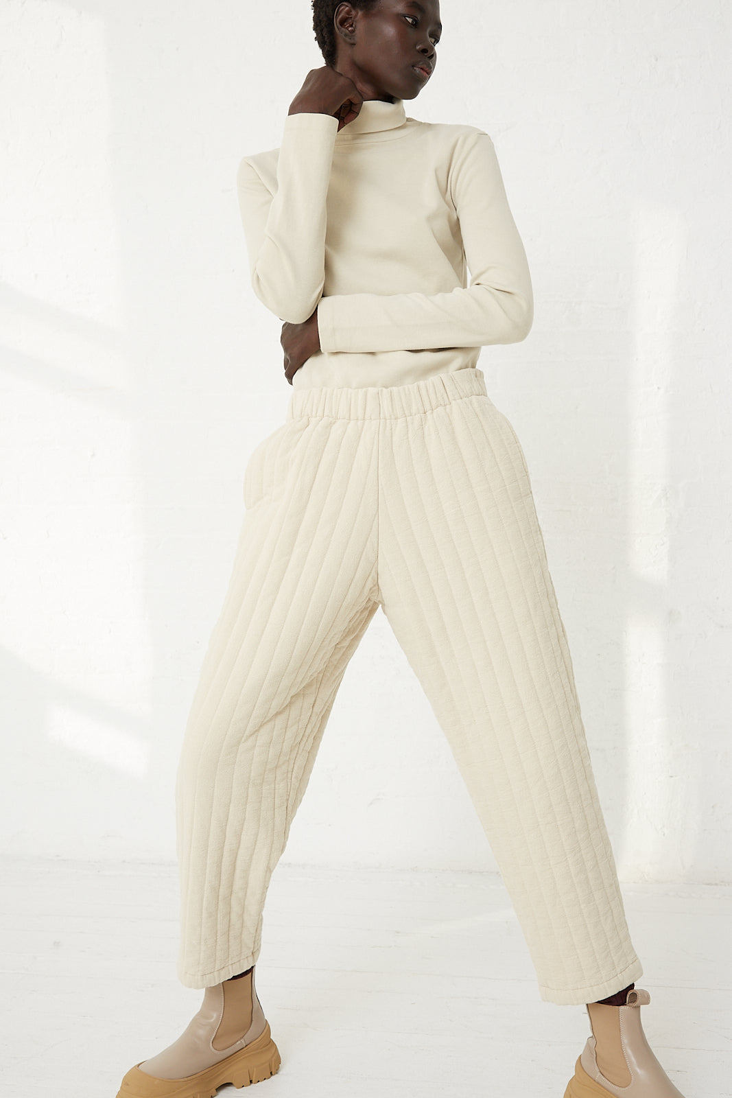 The model is wearing an ivory turtleneck and a pair of Black Crane Quilted Easy Pants in Ivory.