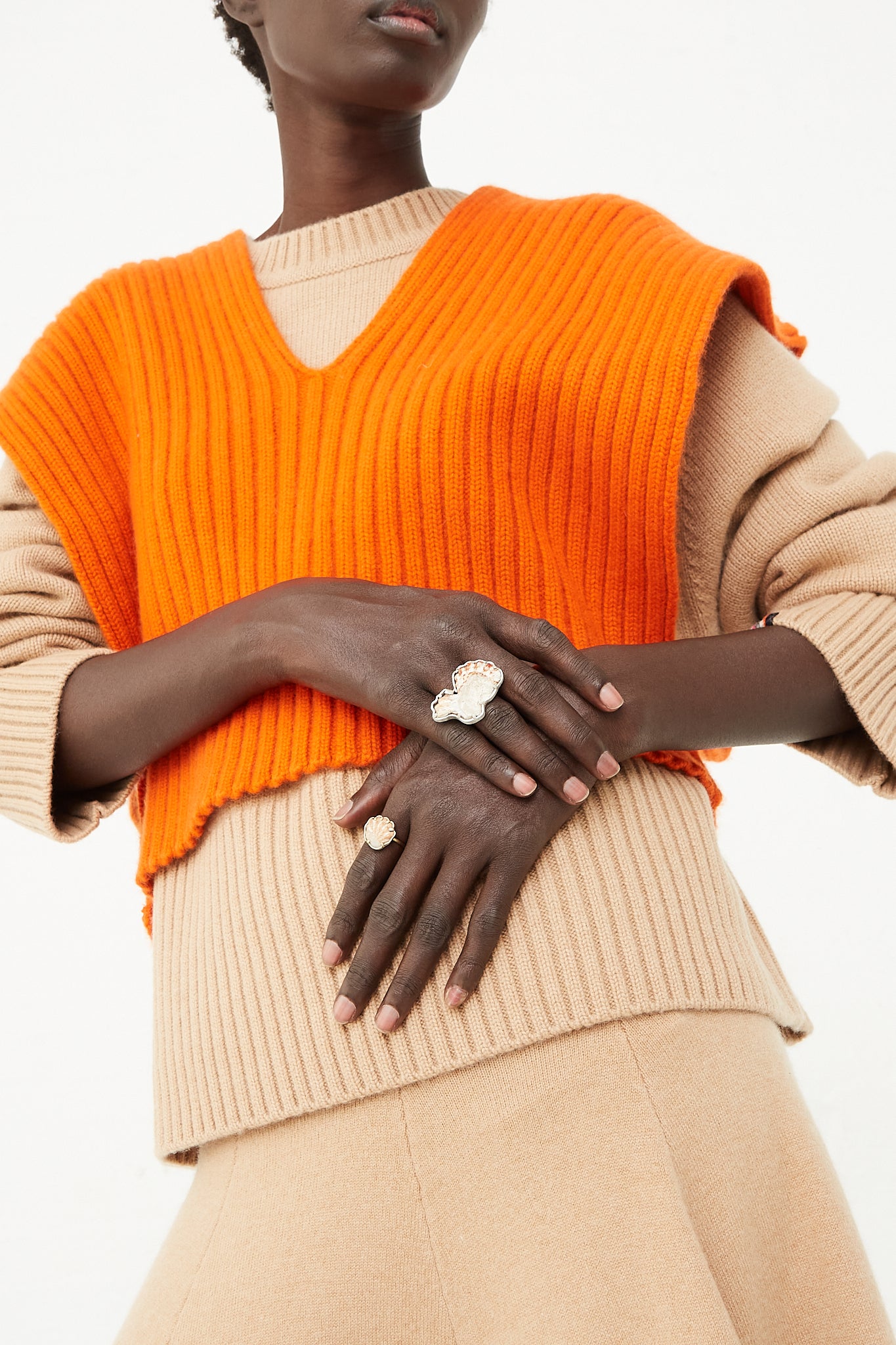 A model wearing an orange sweater and beige skirt showcases La Mar jewelry, specifically the 14K Gold Shell Ring 015, at Oroboro Store.