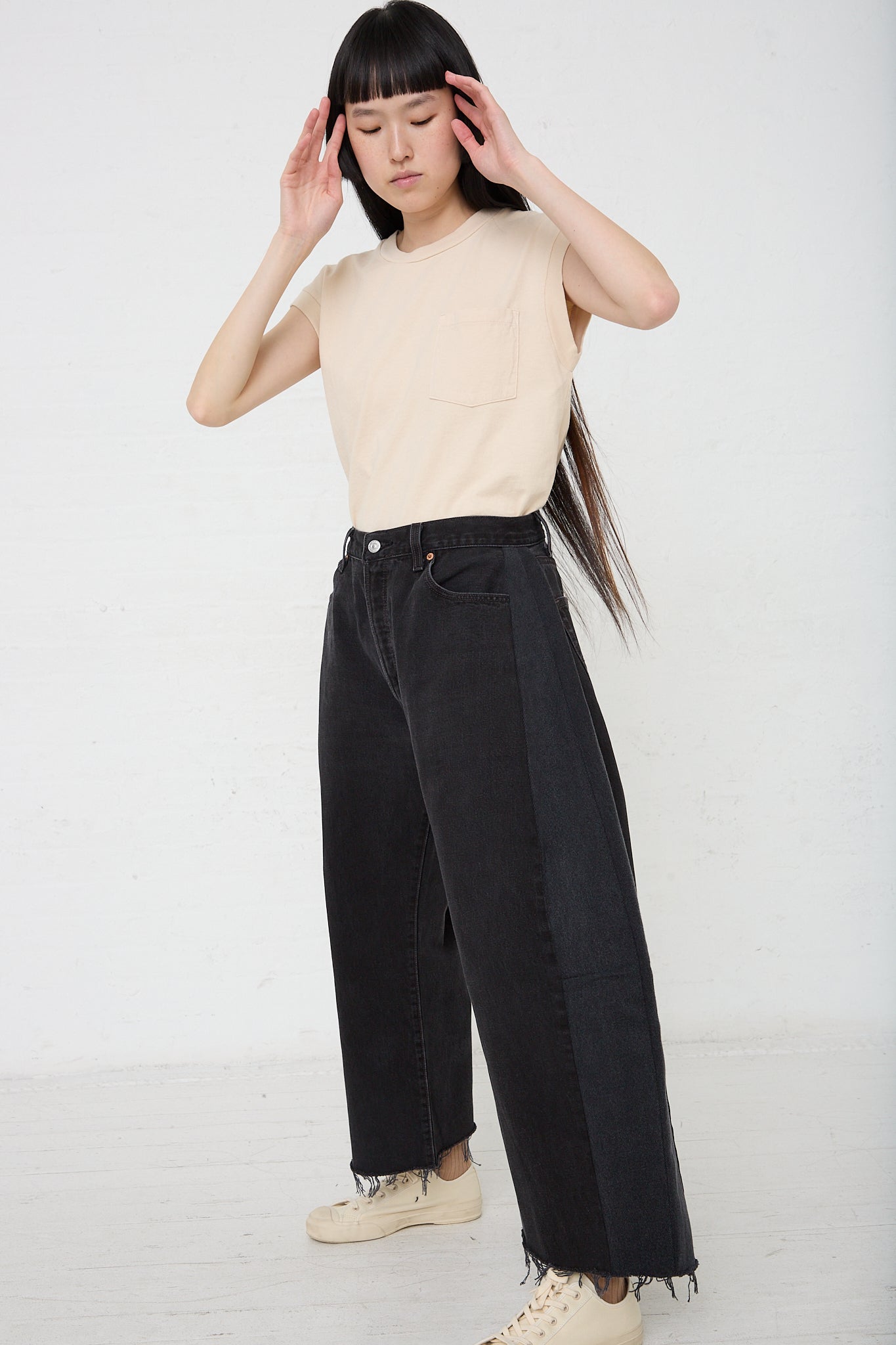 A woman with long hair wearing B Sides' Lasso in Vintage Black denim pants and a beige shirt.